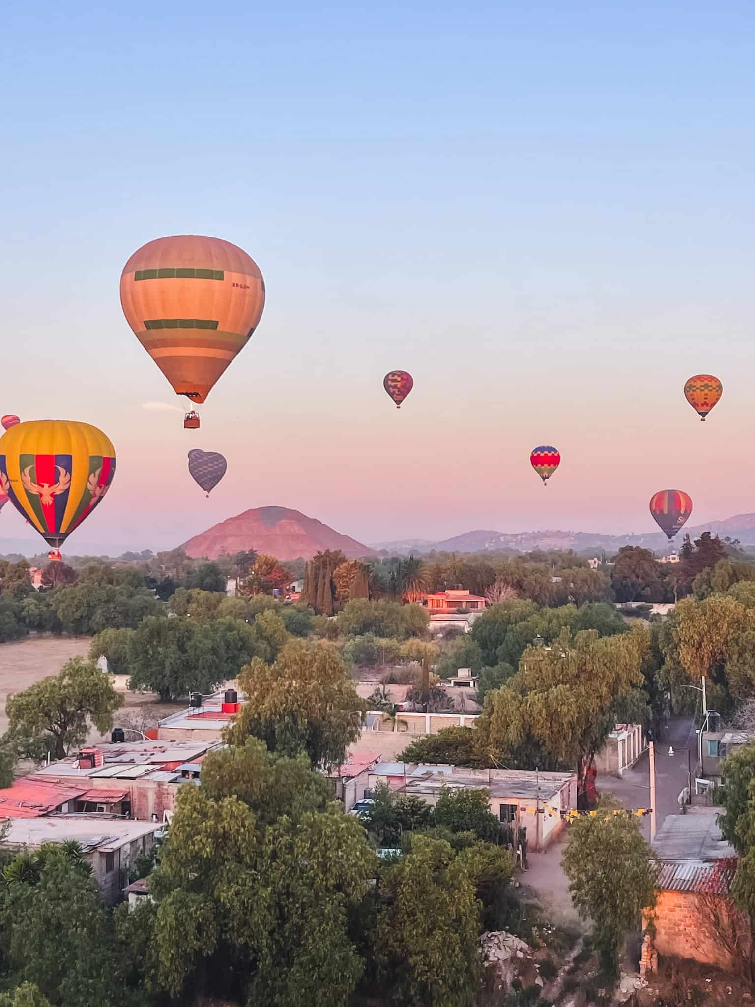 Multiple balloons floating above Teotihuacán with morning haze