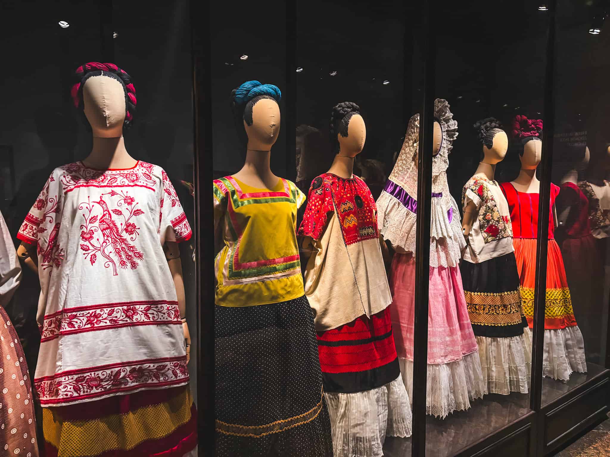 Exhibit of traditional Tehuana dresses worn by Frida Kahlo, showcased in a darkened display room at the Frida Kahlo Blue House.