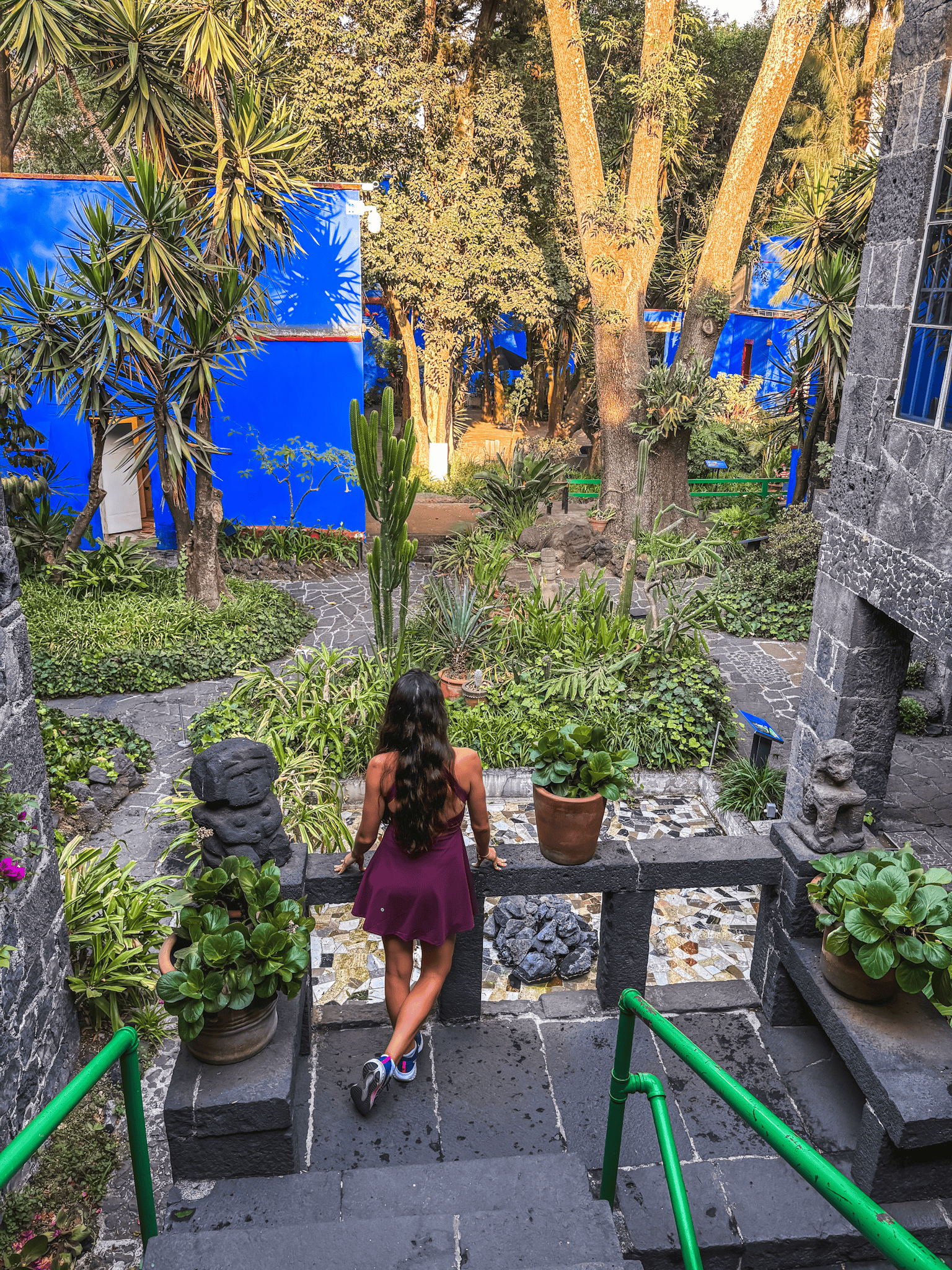 woman in purple dress standing in the gardens of the frida kahlo blue house