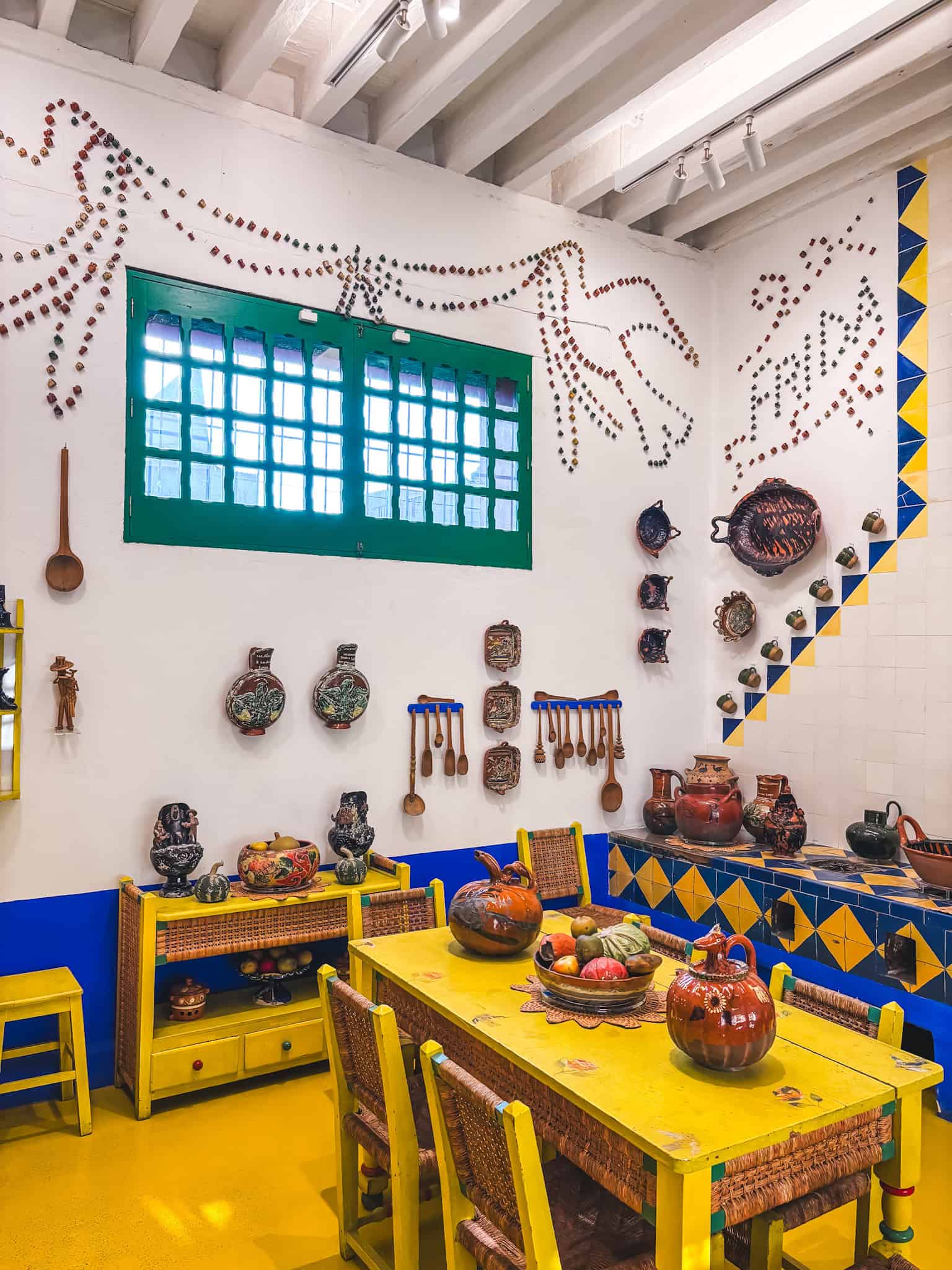 Bright yellow and blue kitchen inside the Frida Kahlo Blue House, decorated with traditional Mexican ceramics and the names “Frida y Diego” spelled out in coffee cups.
