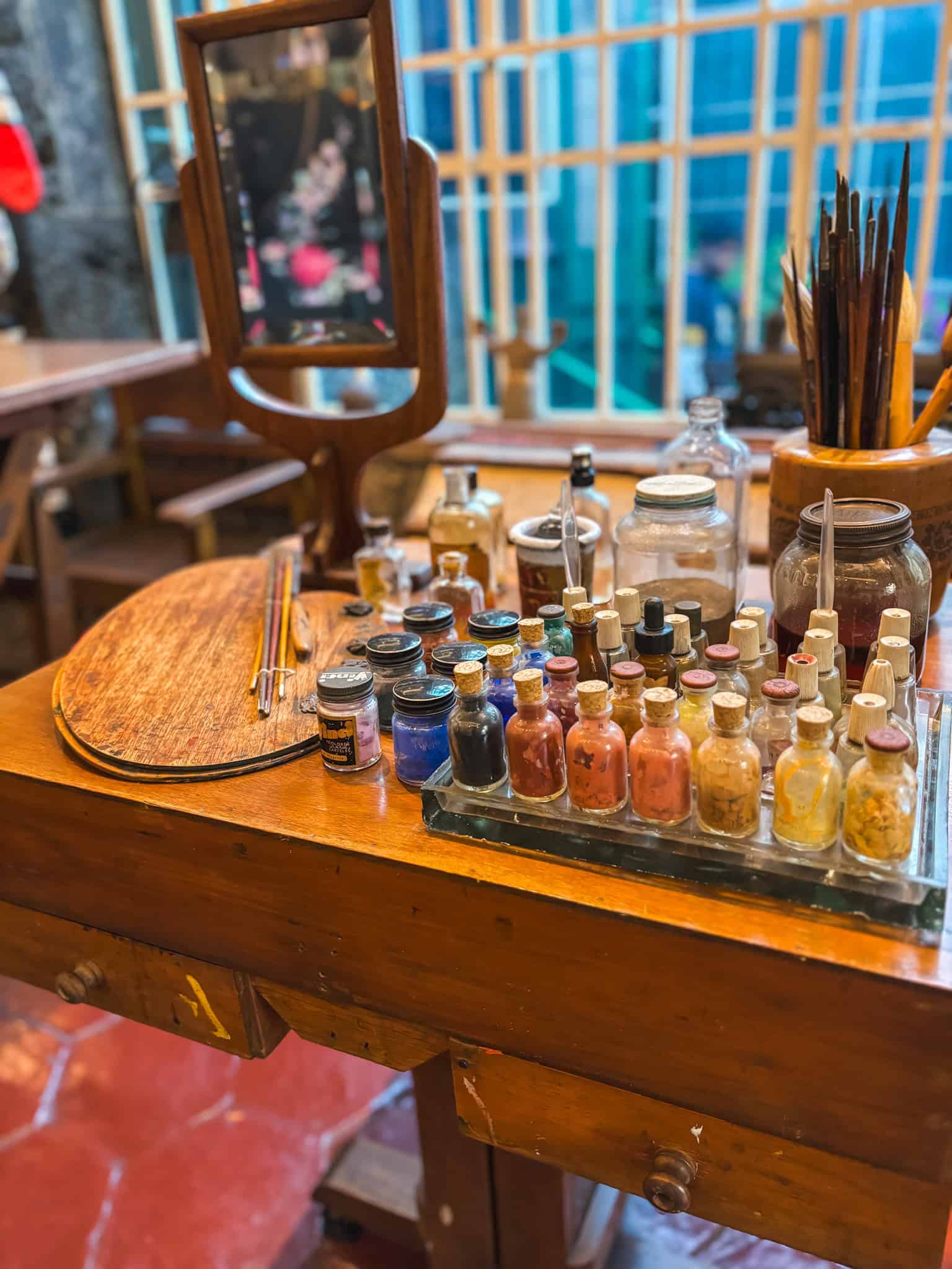 Close-up of Frida Kahlo’s art table in the Frida Kahlo Blue House, featuring pigments, jars, brushes, and a wooden palette.
