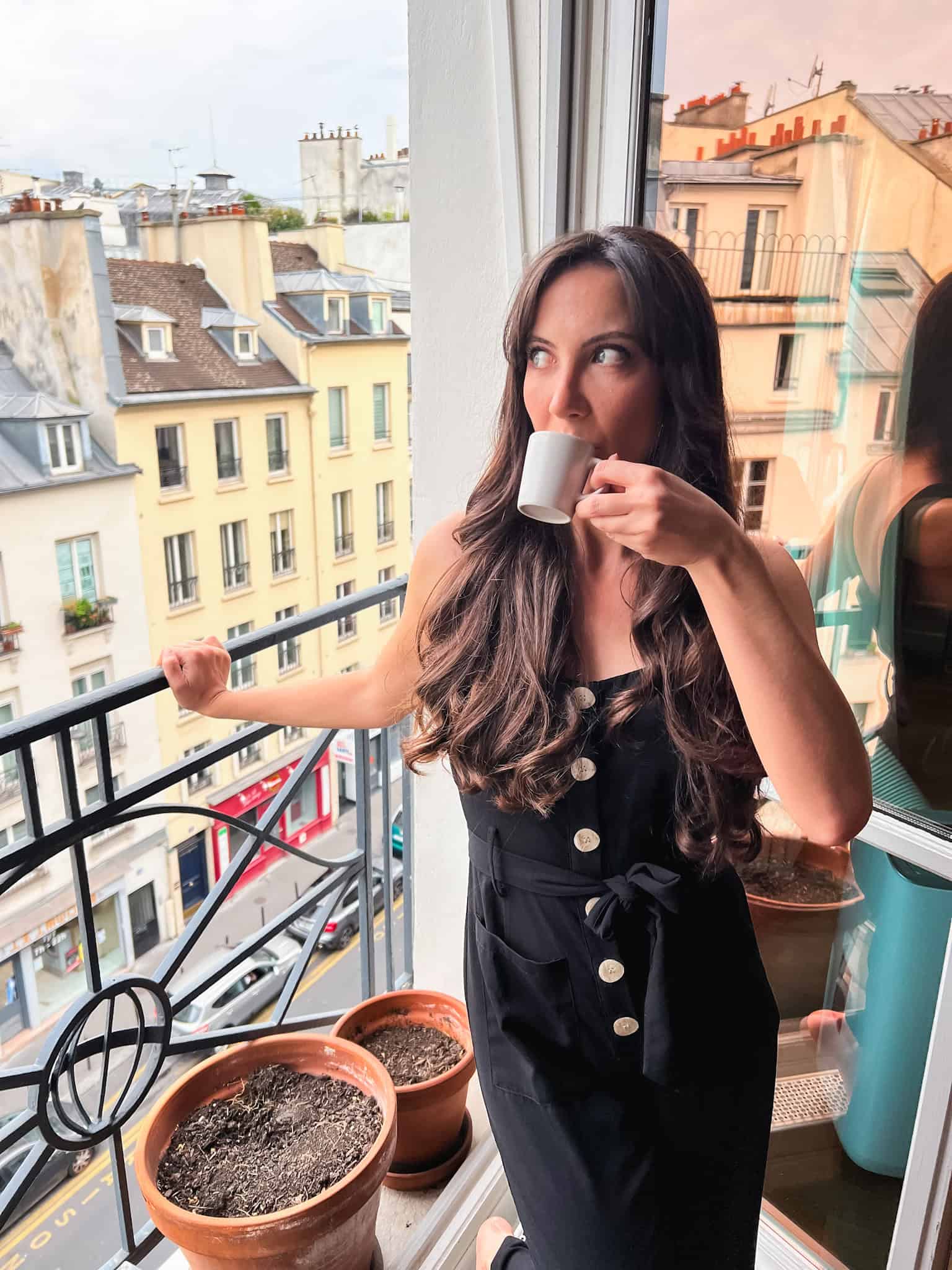Woman sipping coffee on a Parisian balcony with colorful rooftops in the background, showcasing the morning ritual tied to the best coffee shops in Paris.