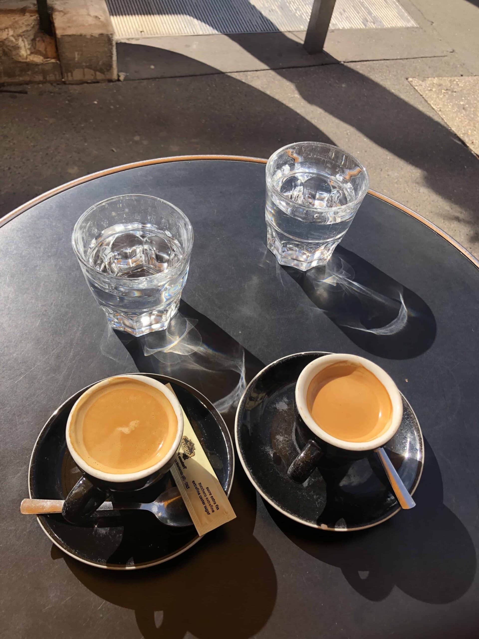 Two espresso shots with glasses of water on a round café table in the sun, capturing the minimalist vibe of the best coffee shops in Paris.