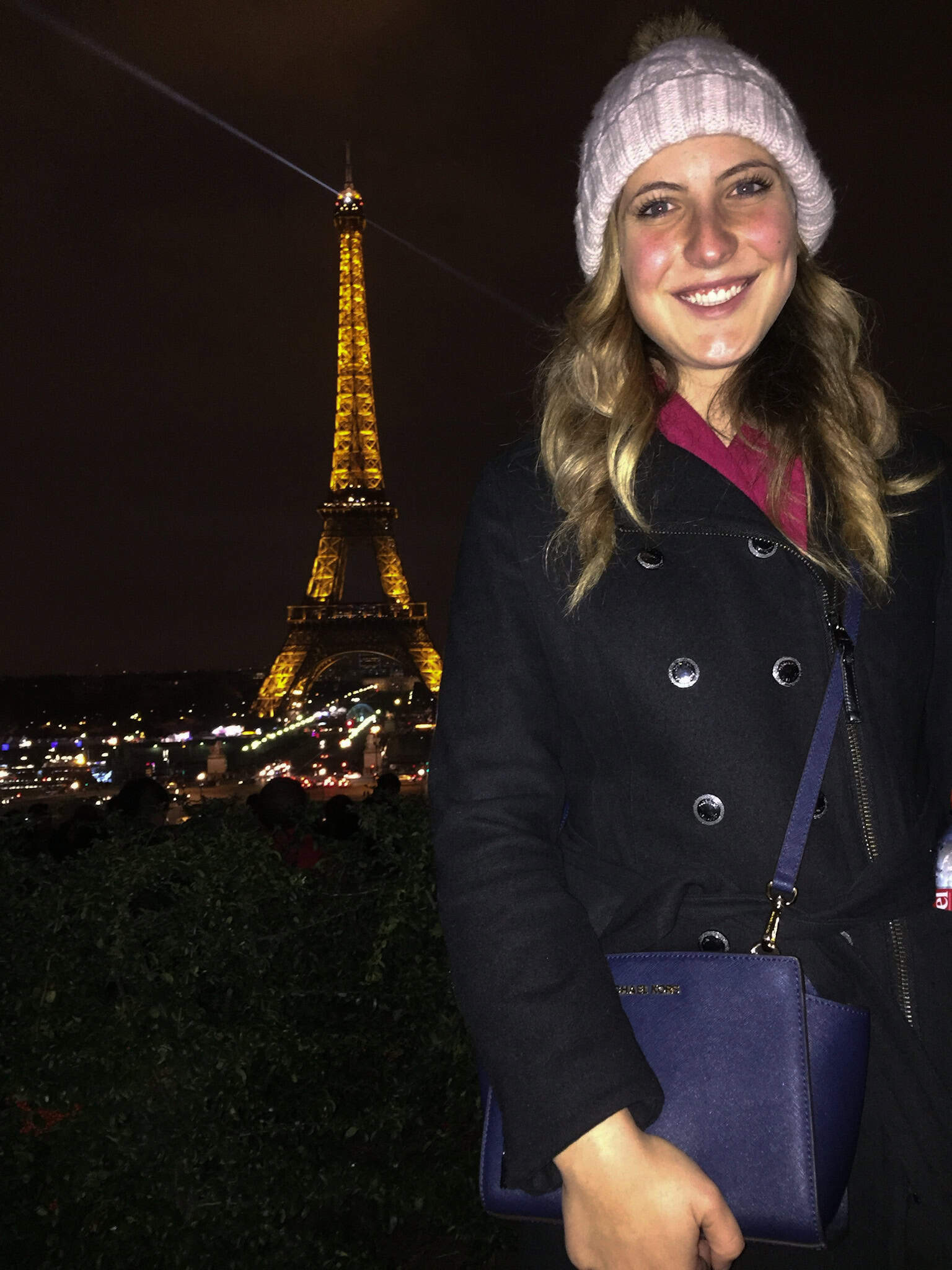 Smiling in a pink hat with the Eiffel Tower sparkling behind—celebrating a perfect night in Paris in winter.