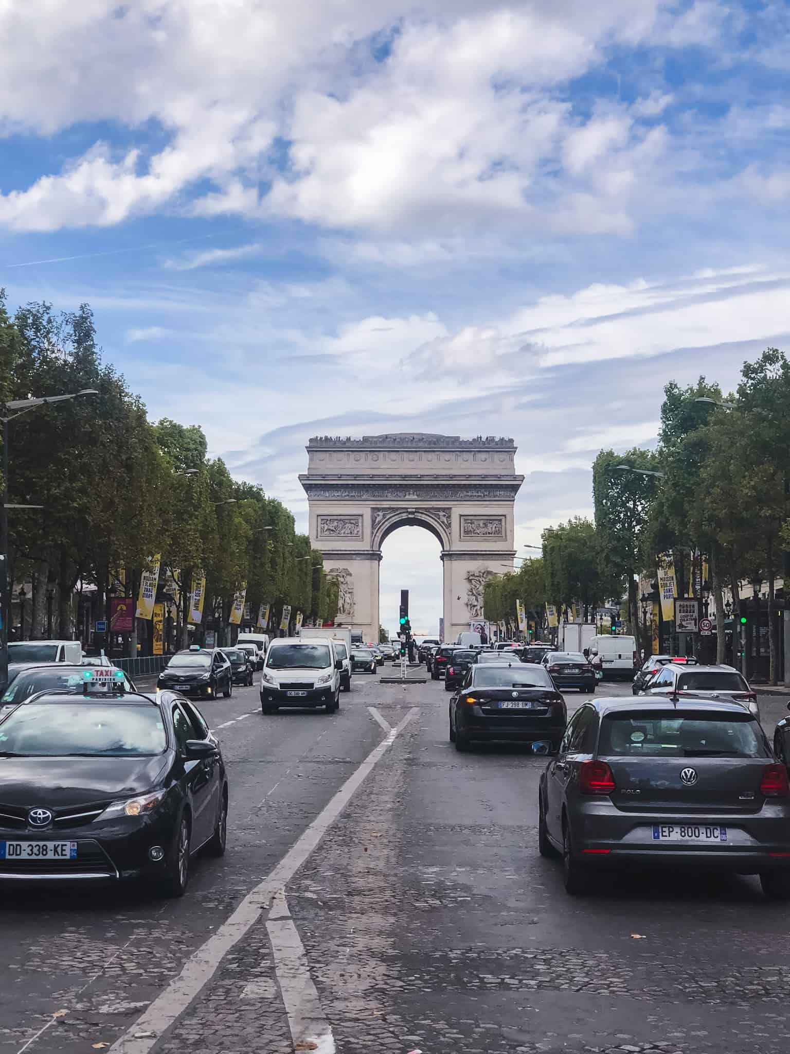 Arc de Triomphe seen from the Champs-Élysées with traffic in the foreground on a partly cloudy day in Paris.