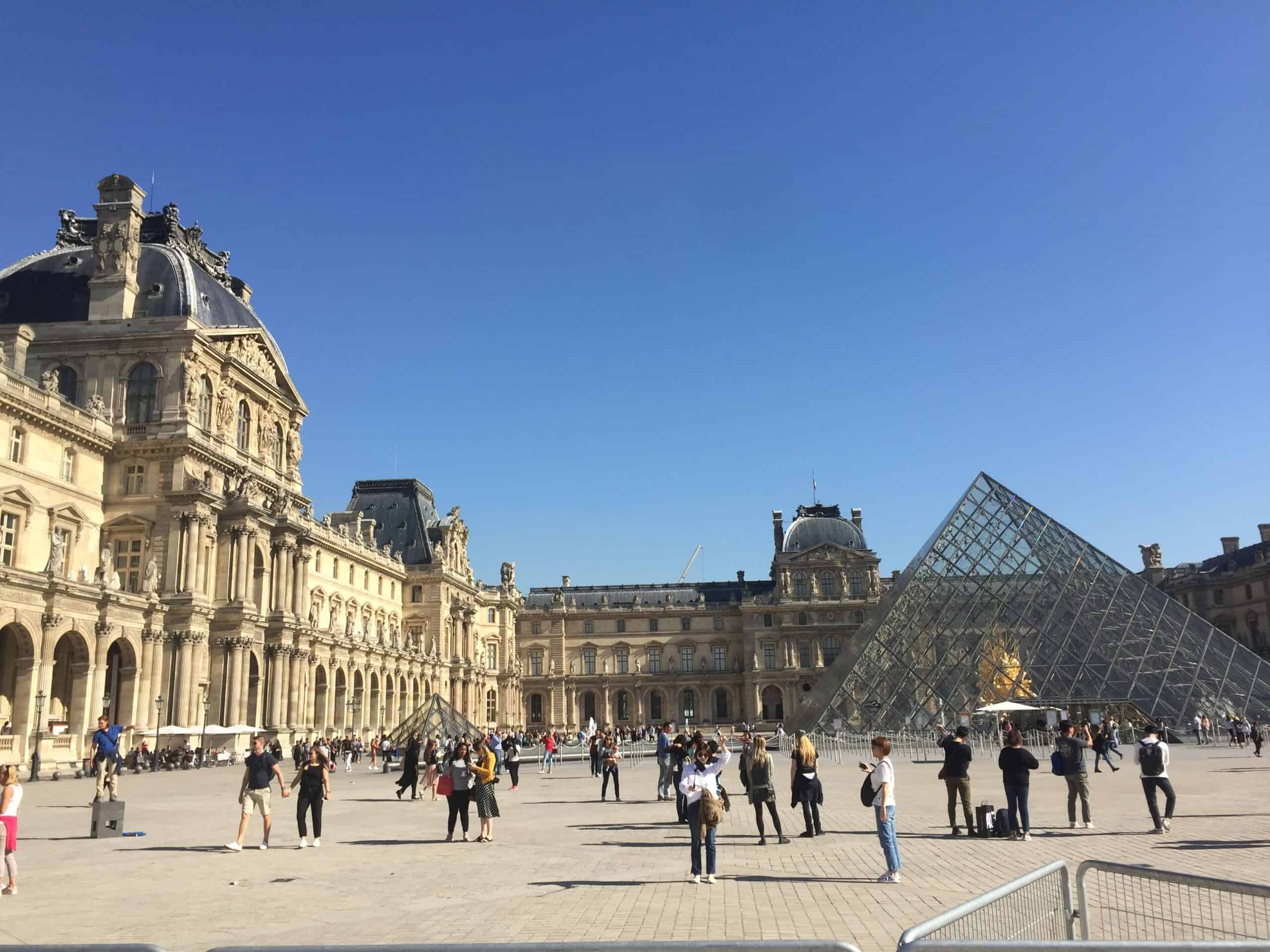 Courtyard of the Louvre Museum with glass pyramid and historic architecture under a clear blue sky, one of the highlights of 3 days in Paris.