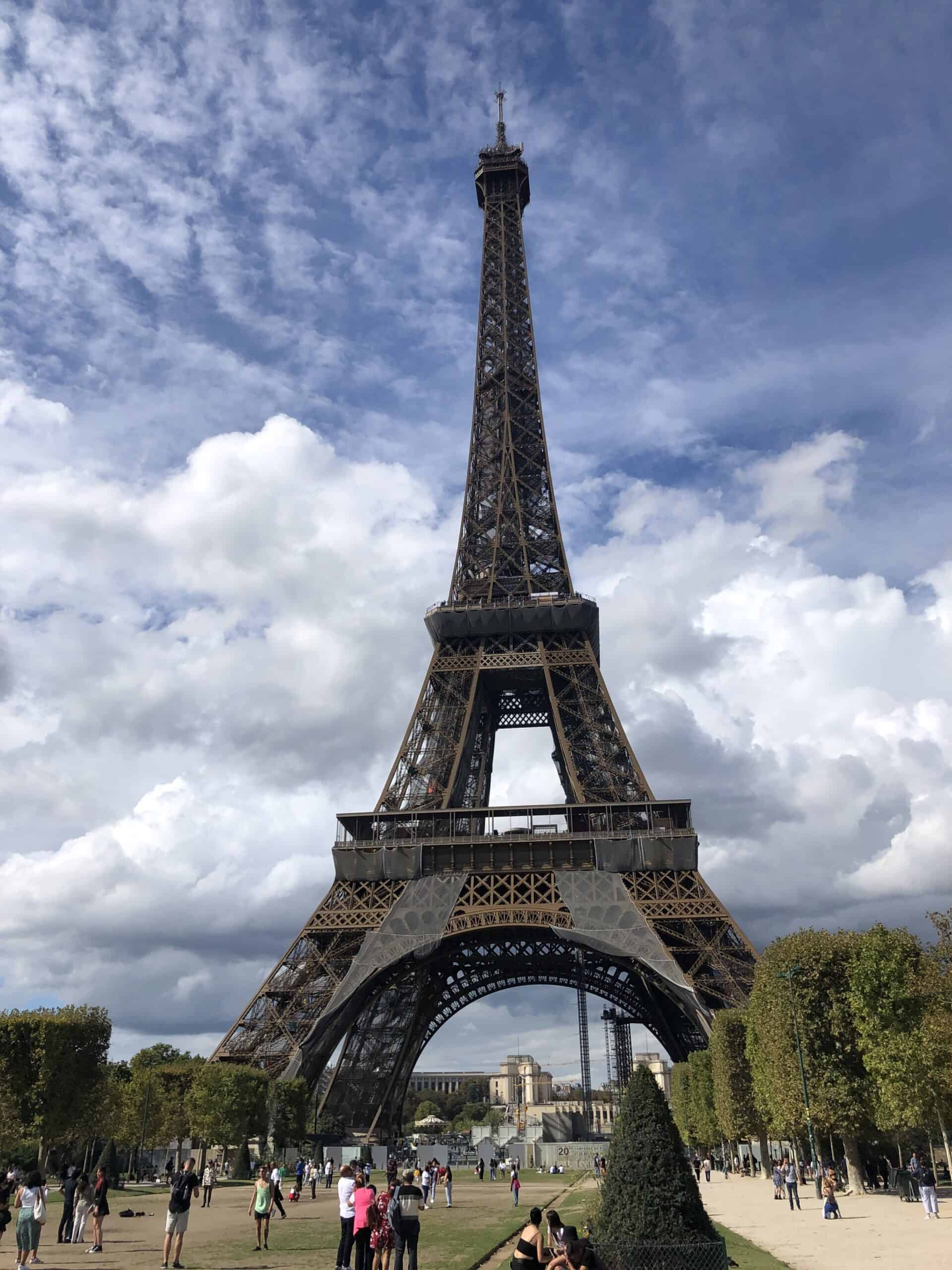 Eiffel Tower from the Champ de Mars on a partly cloudy day, surrounded by visitors capturing the perfect Paris memory.