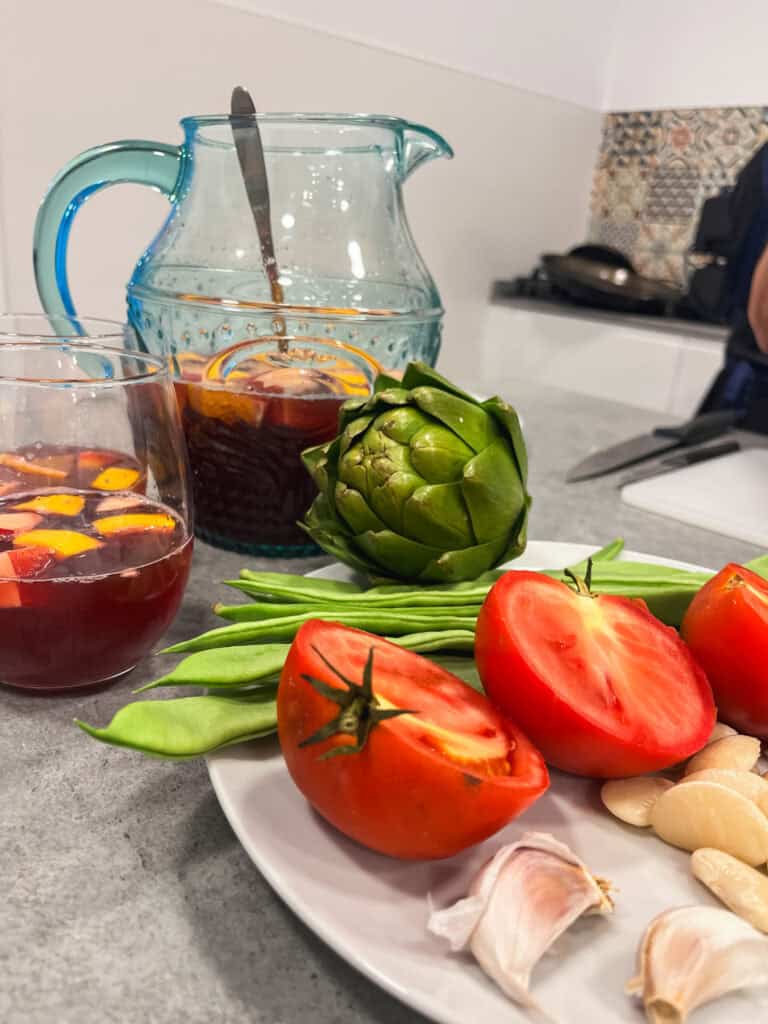 Fresh Spanish ingredients including ripe tomatoes, artichoke, garlic and sangria pitcher - essential elements of a Malaga cooking class