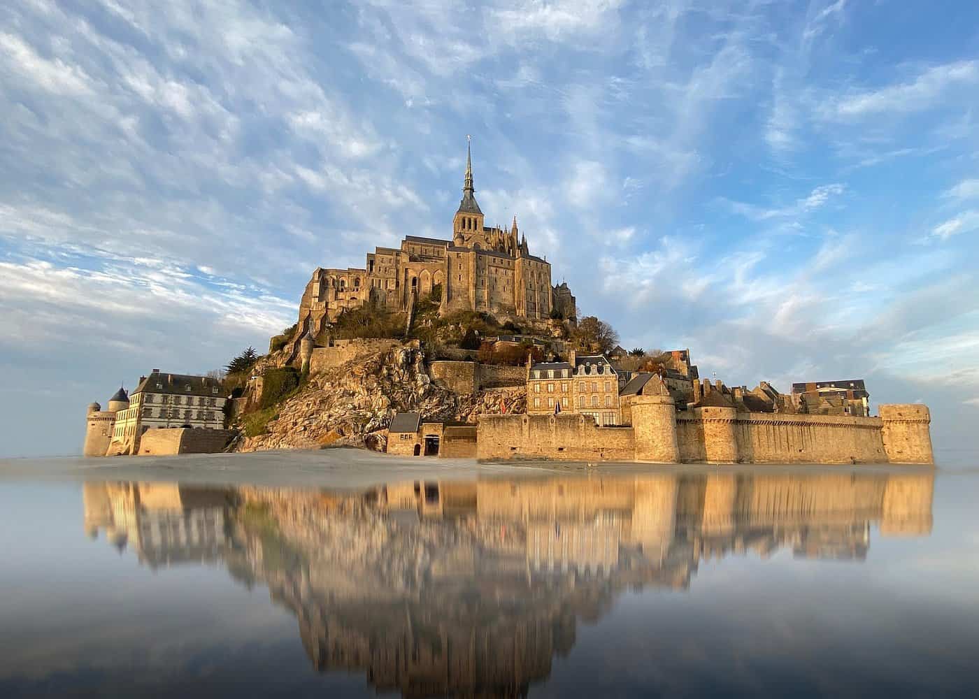Stunning reflection of Mont Saint-Michel abbey at golden hour, showcasing this UNESCO World Heritage site and popular day trips from Paris destination