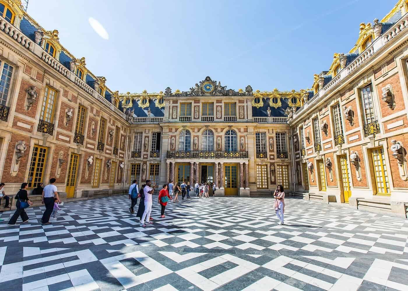 Tourists exploring the magnificent marble courtyard of Palace of Versailles, a must-see destination for day trips from Paris