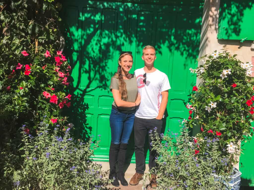 Couple posing at Monet's house in Giverny with iconic green shutters and blooming flower garden