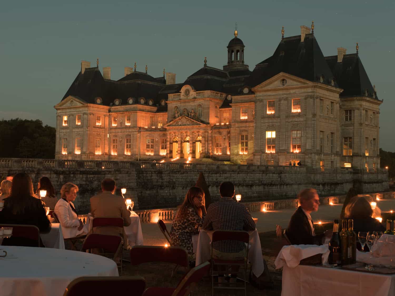 Château de Vaux-le-Vicomte illuminated at night with candlelit outdoor dining, a magical destination for day trips from Paris by train