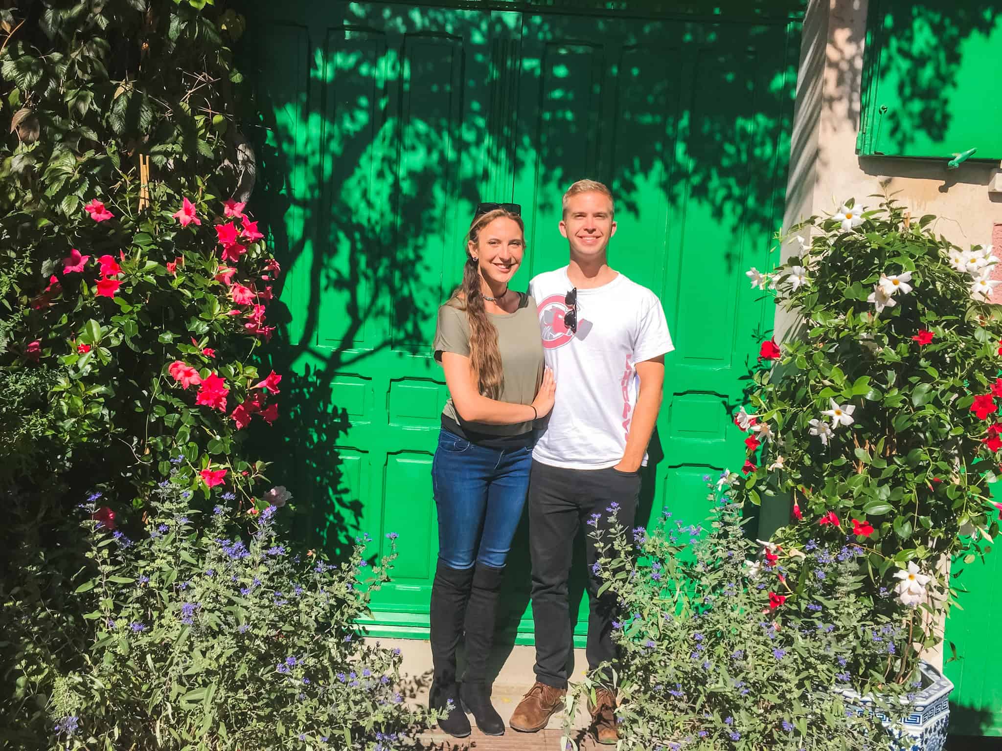 Couple posing at Claude Monet's house in Giverny, one of the most popular day trips from Paris, with the iconic green door and colorful flower gardens