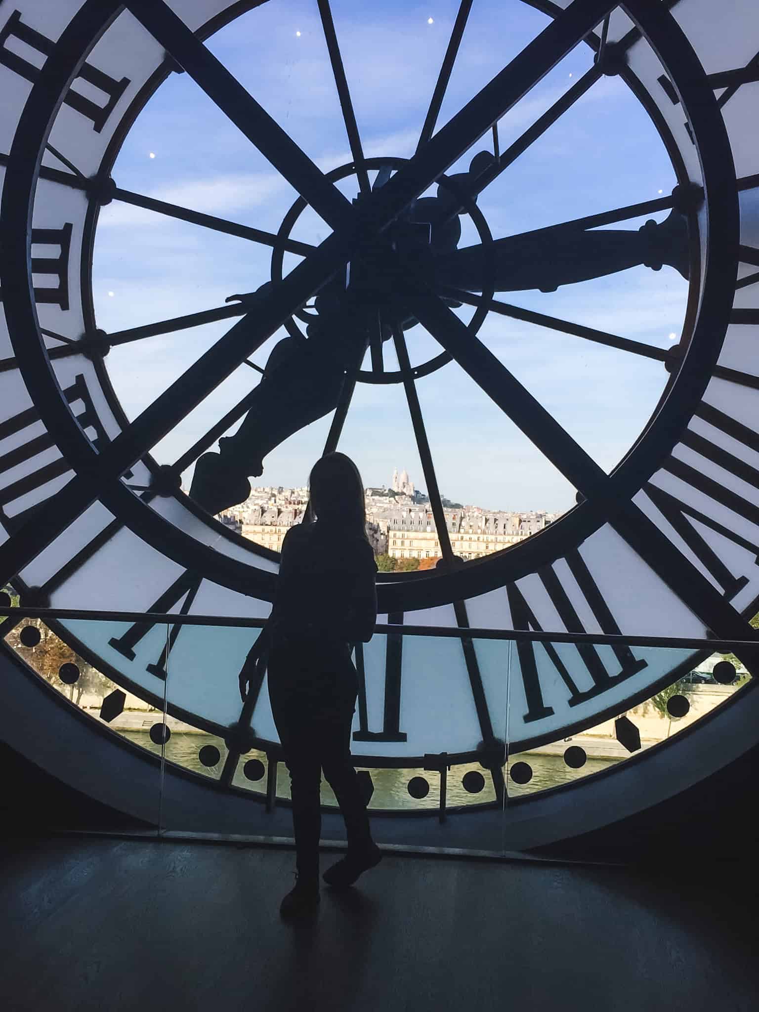 Silhouette of visitor standing behind famous clock window at Musée d'Orsay overlooking Paris skyline