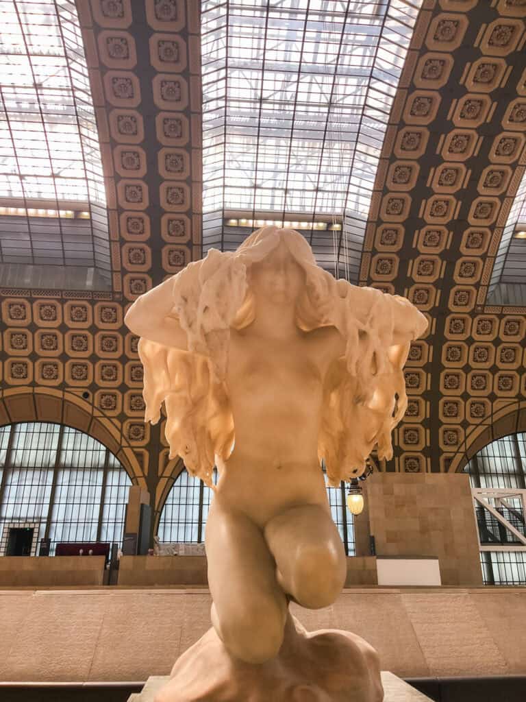 Classical marble statue displayed under glass ceiling at Musée d'Orsay train station museum in Paris
