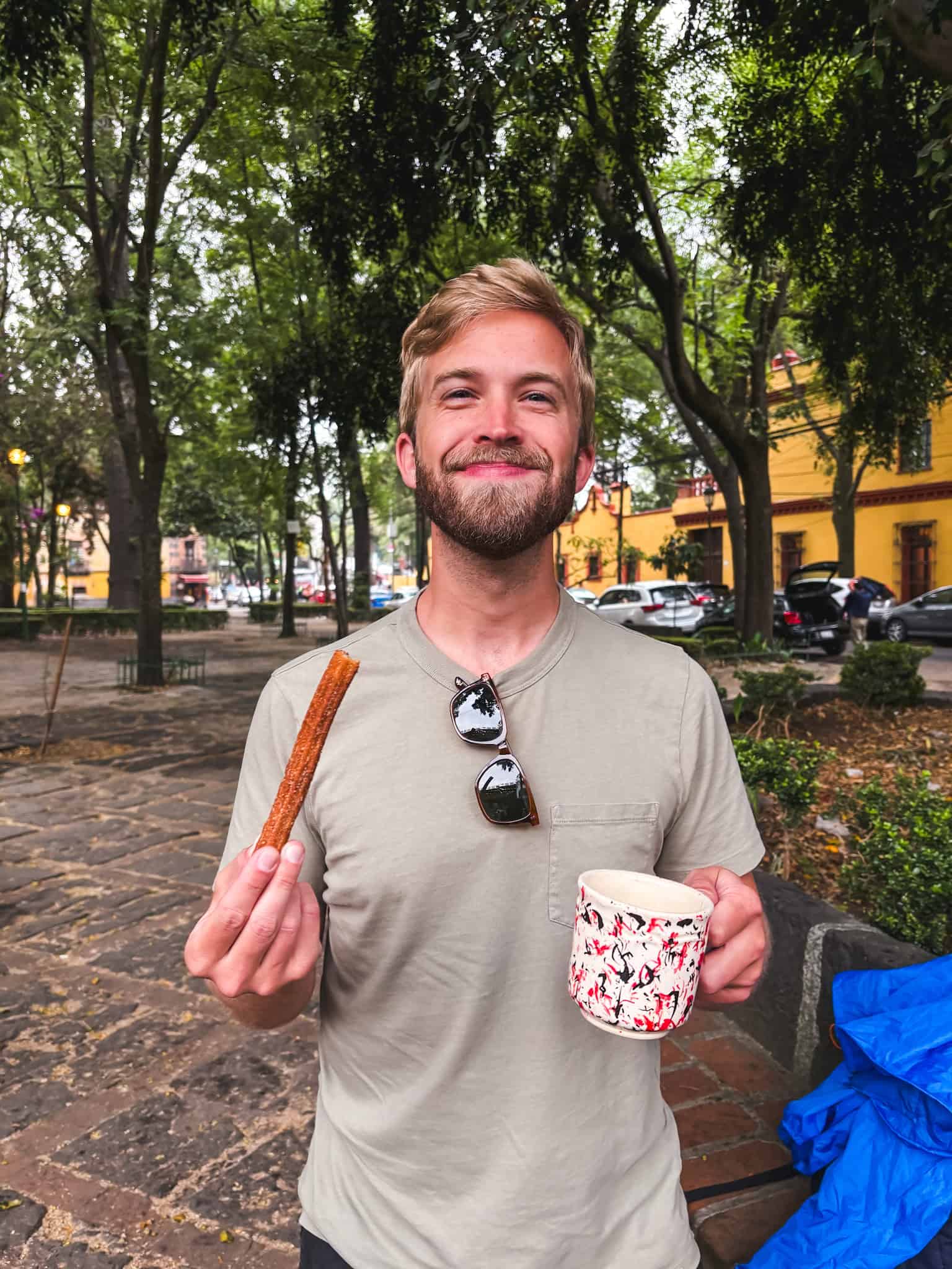 Man holding churro and hot chocolate cup while standing in cobblestone square, showcasing what to do in Mexico City for food experiences