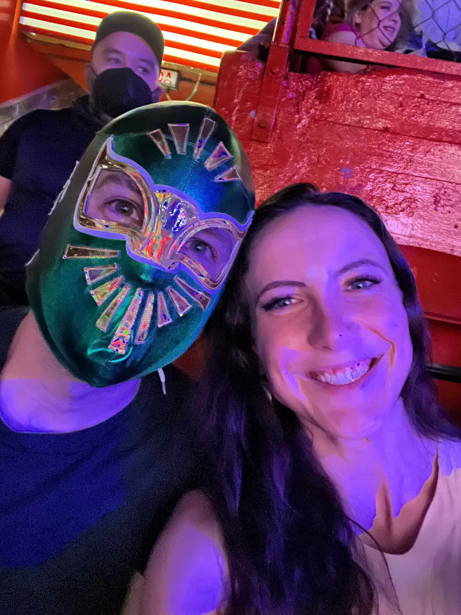Two people wearing lucha libre wrestling masks taking selfie at colorful arena
