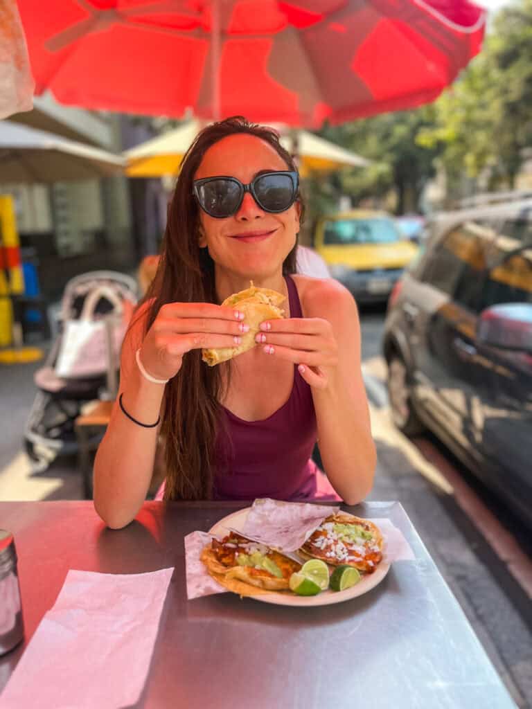 Woman eating street tacos at outdoor table under red umbrella in Mexico City