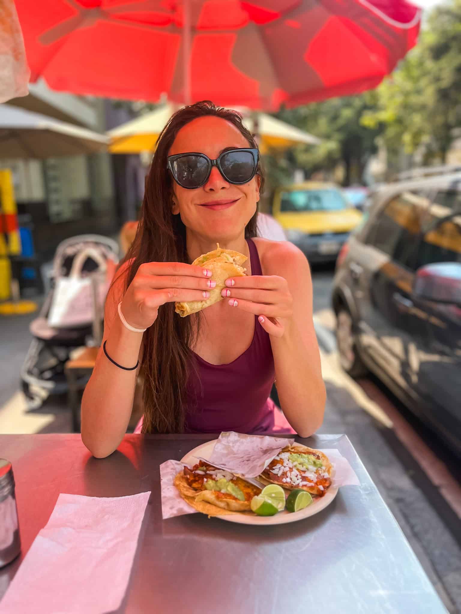 Woman eating street tacos at outdoor table under red umbrella in Mexico City