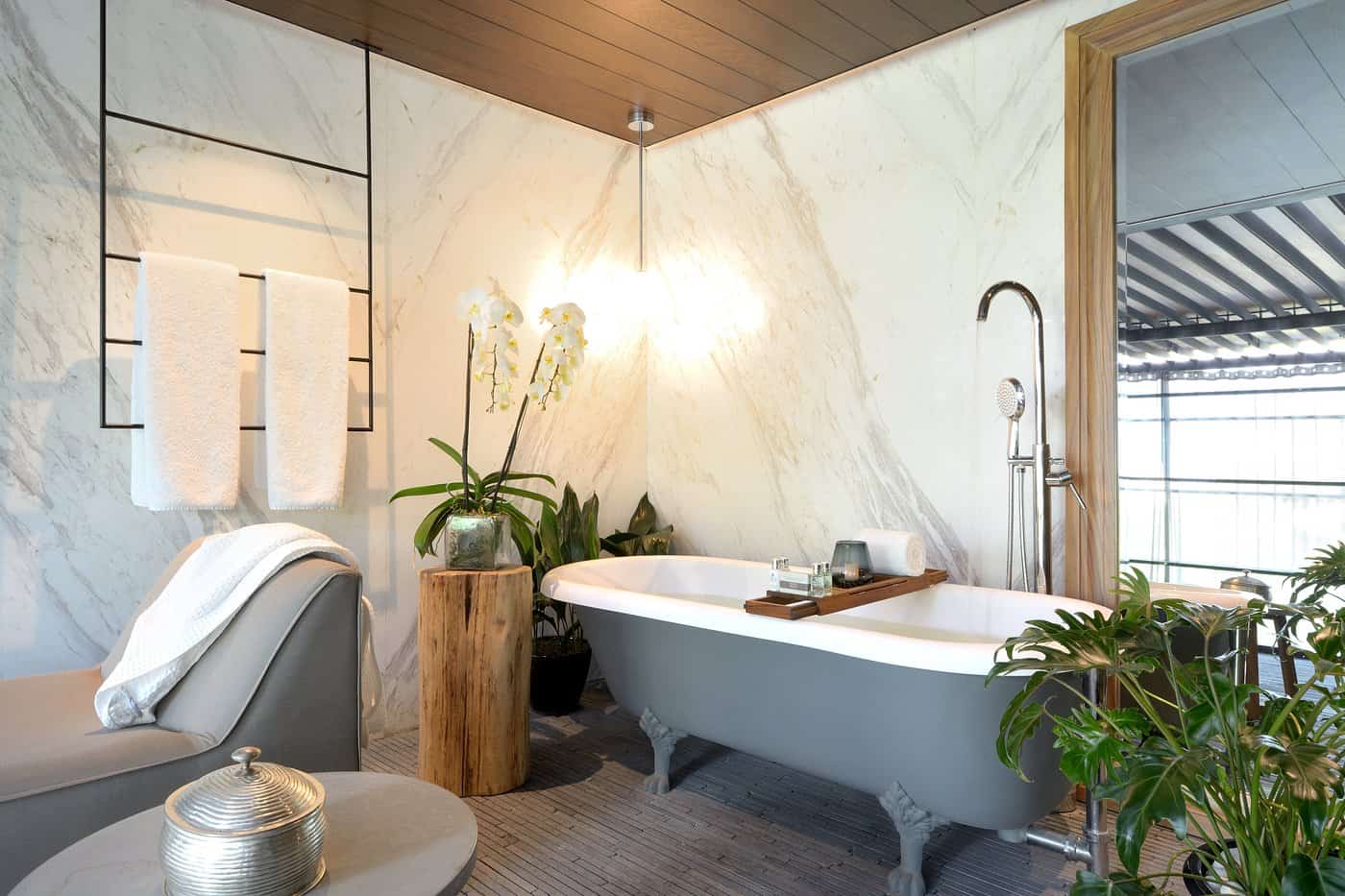Luxurious spa bathroom with white clawfoot bathtub, marble walls, wooden ceiling, and plants at the high-end Mexico City Brick hotel during the best time to visit Mexico City for a relaxing getaway