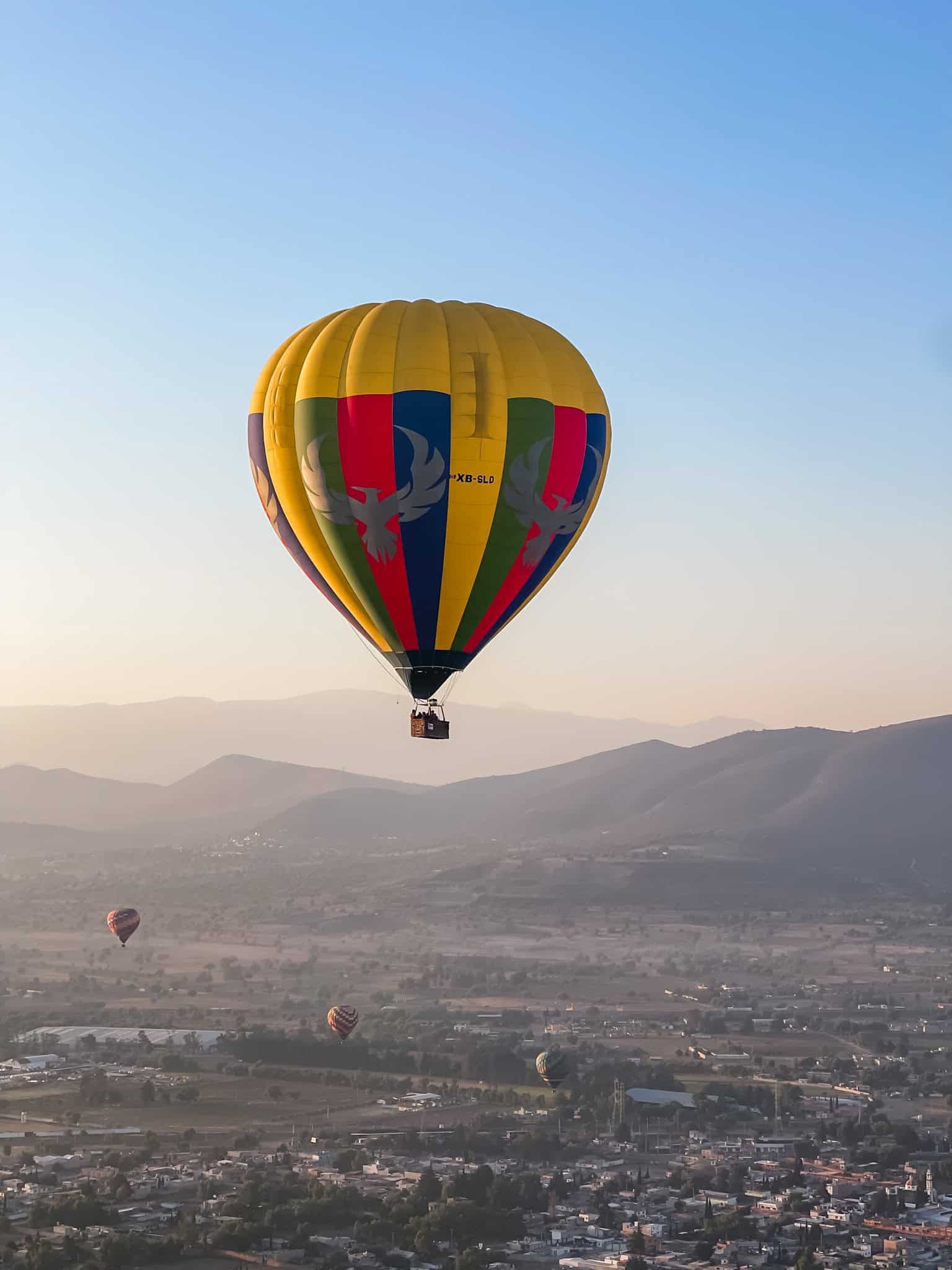 Colorful hot air balloon floating over the Teotihuacan valley during the best time to visit Mexico City, with mountains and additional balloons visible in the clear morning sky