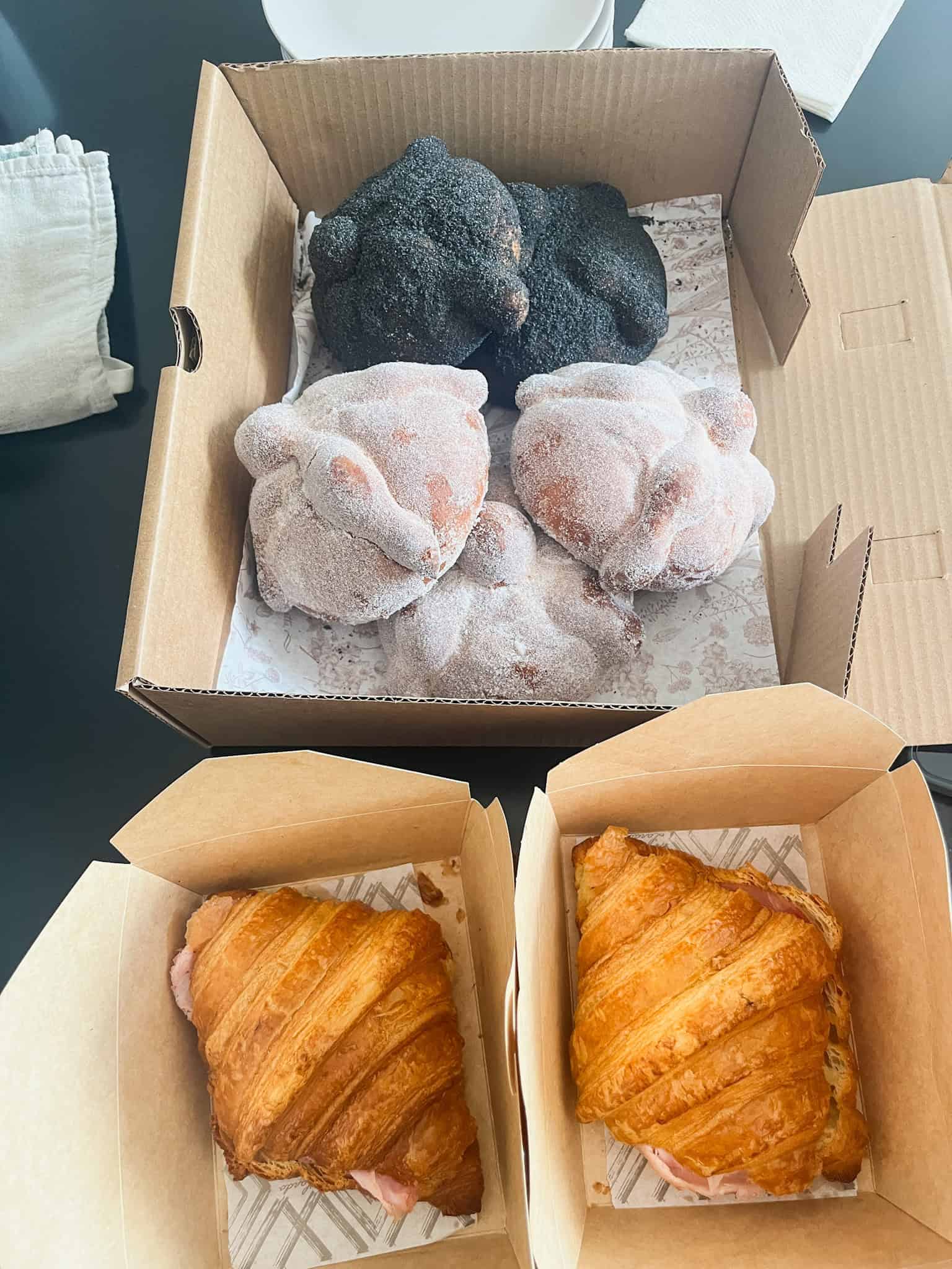 Assorted Mexican pastries and baked goods in takeout boxes, including chocolate-covered treats and golden flaky croissants, showcasing Mexico City's incredible bakery scene