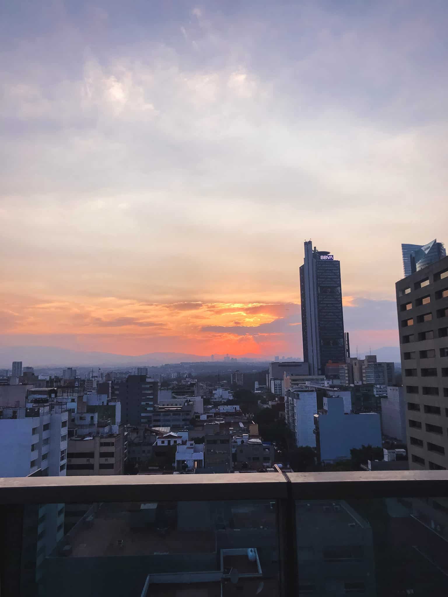 Golden sunset over Mexico City skyline viewed from a rooftop terrace during the best time to visit Mexico City, with BBVA tower and buildings silhouetted against orange and pink sky