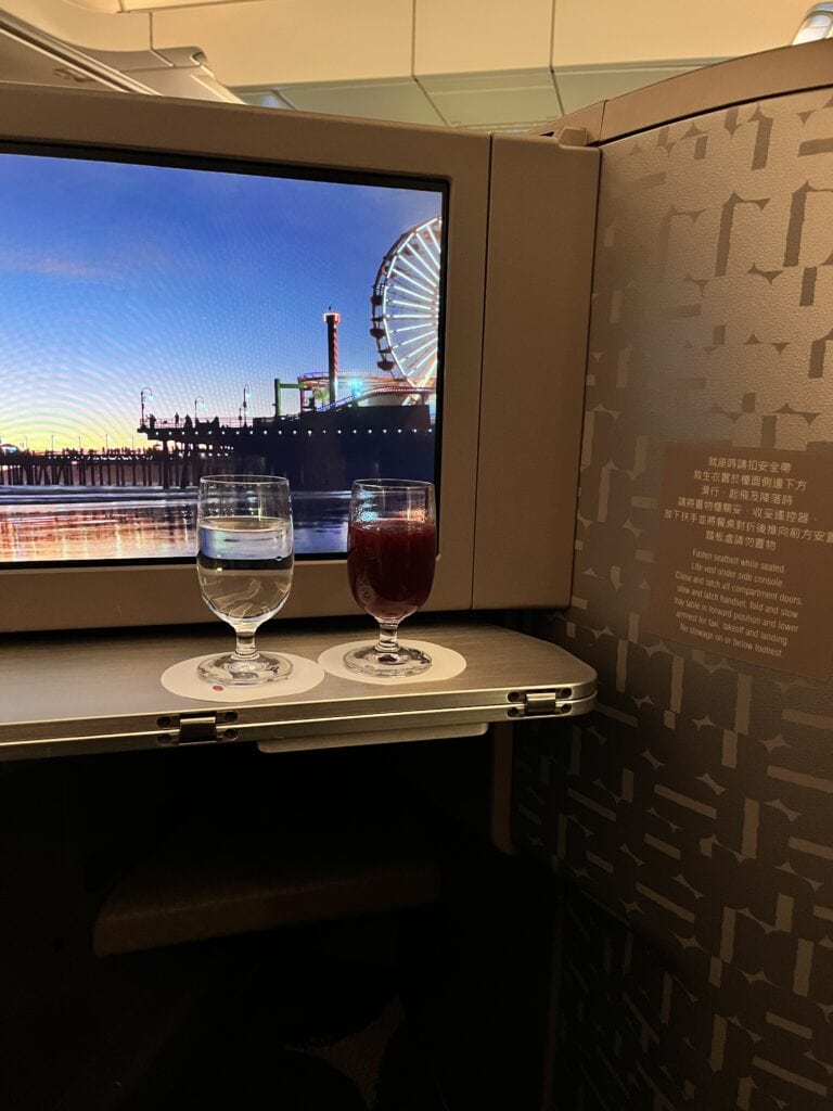 Premium beverages served on tray table with entertainment screen displaying Santa Monica pier ferris wheel