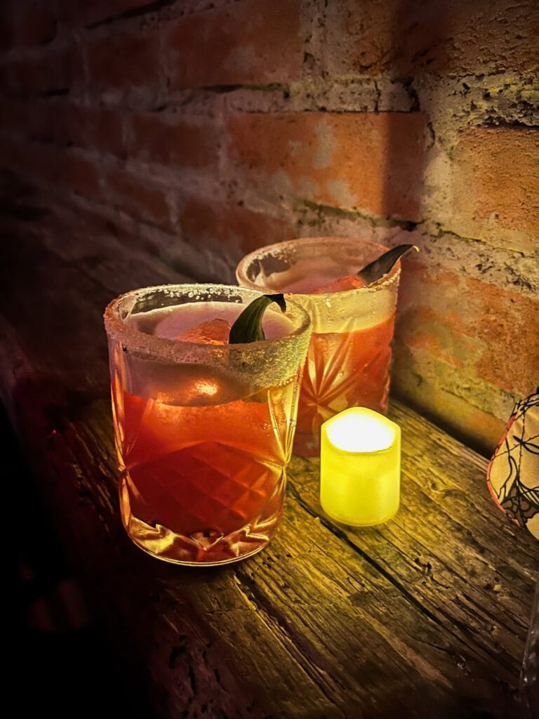 Artisanal mezcal cocktails in atmospheric bar setting, illustrating the nightlife scene that both attracts visitors and concerns Mexico City protest participants worried about gentrification