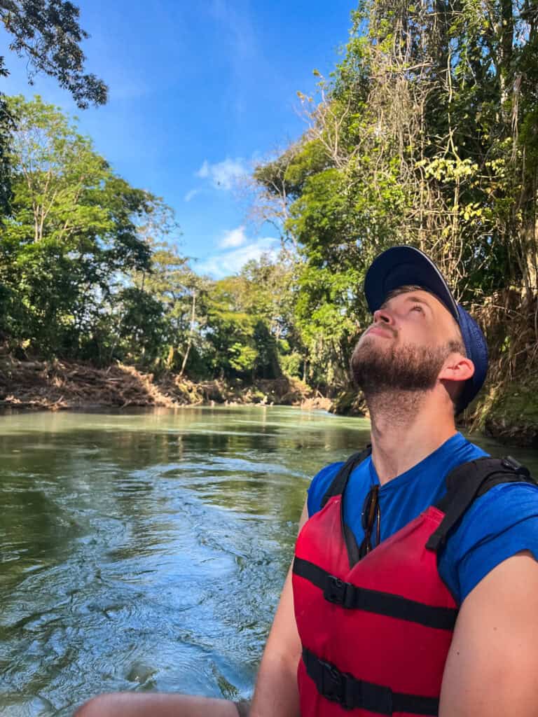 Tourist in life vest looking up at rainforest canopy from river during wildlife float tour