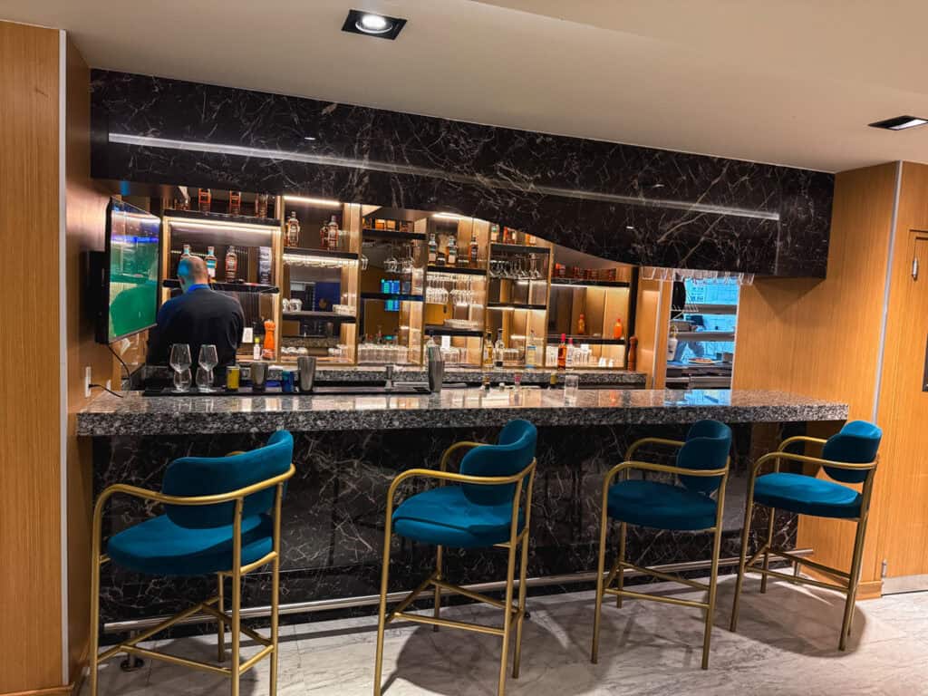 Interior bar area of the Centurion lounge Mexico City featuring blue velvet bar stools, black marble bar top, and well-stocked liquor display