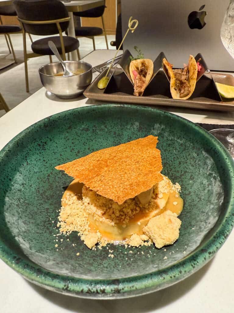Plated food presentation showing tacos in metal holders and an elegant dessert with tuile garnish on green speckled ceramic plates