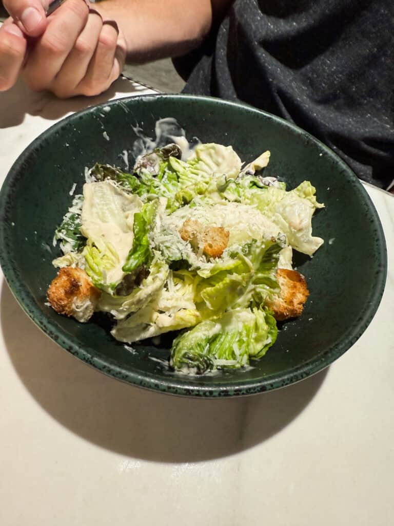 Caesar salad with romaine lettuce, croutons, and parmesan cheese served in green ceramic bowl at the lounge