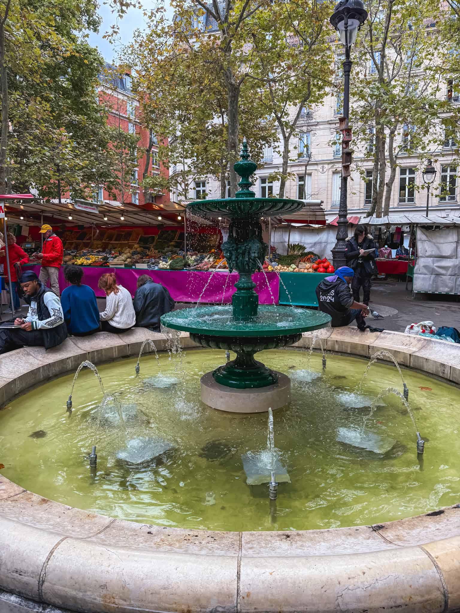 Traditional green fountain at Paris street market with vendors and shoppers