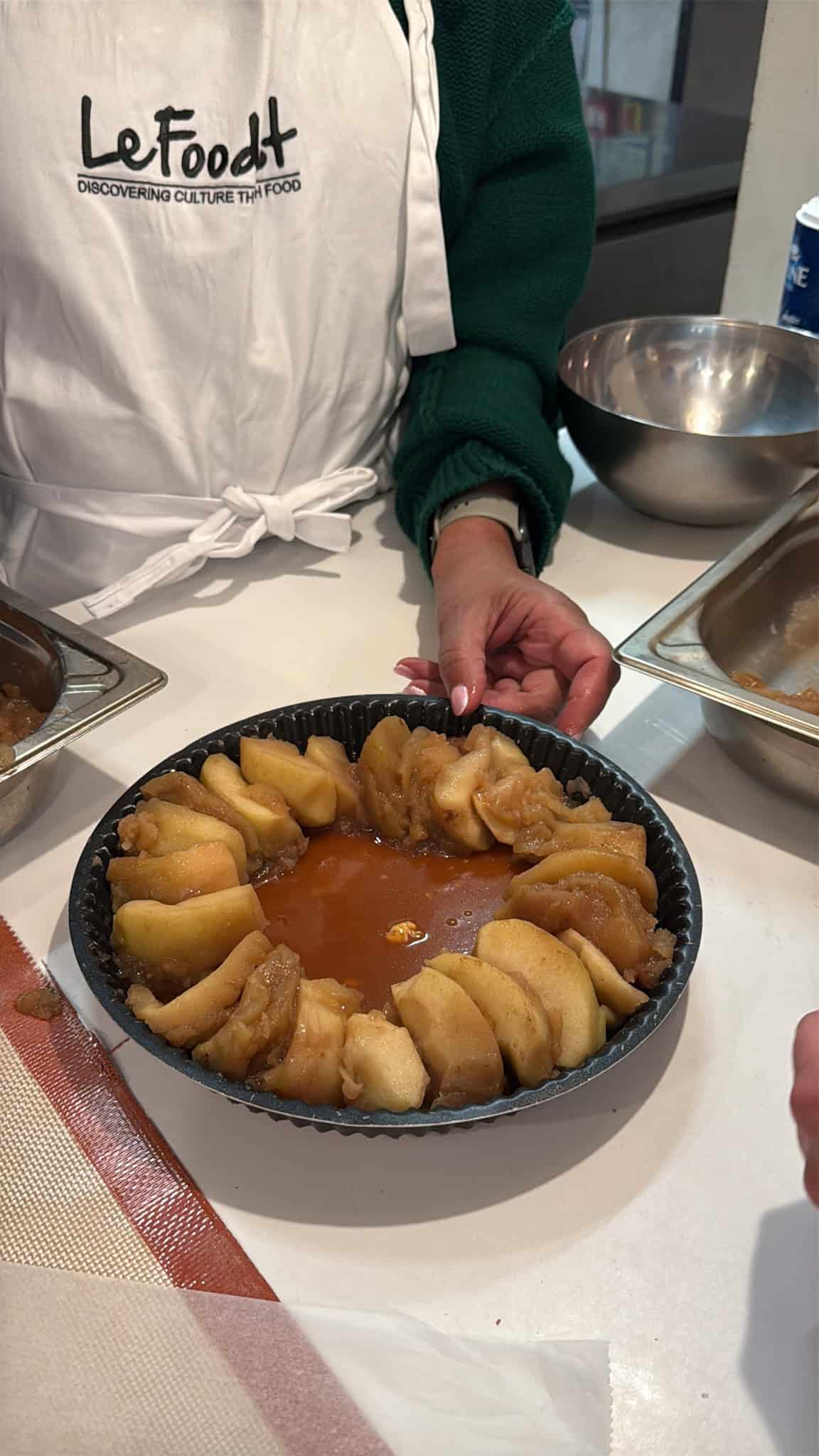 Student arranging caramelized apple slices in tart pan during cooking class in Paris