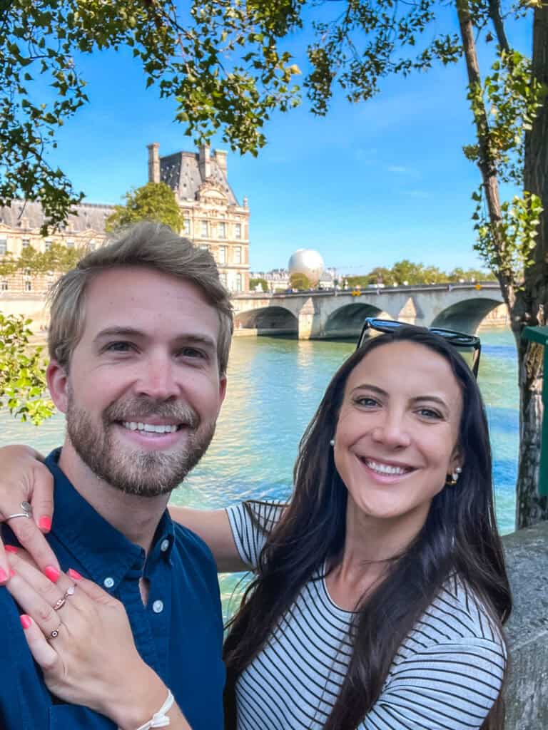 Couple enjoying romantic things to do in Paris along the Seine River with the Louvre palace in the background