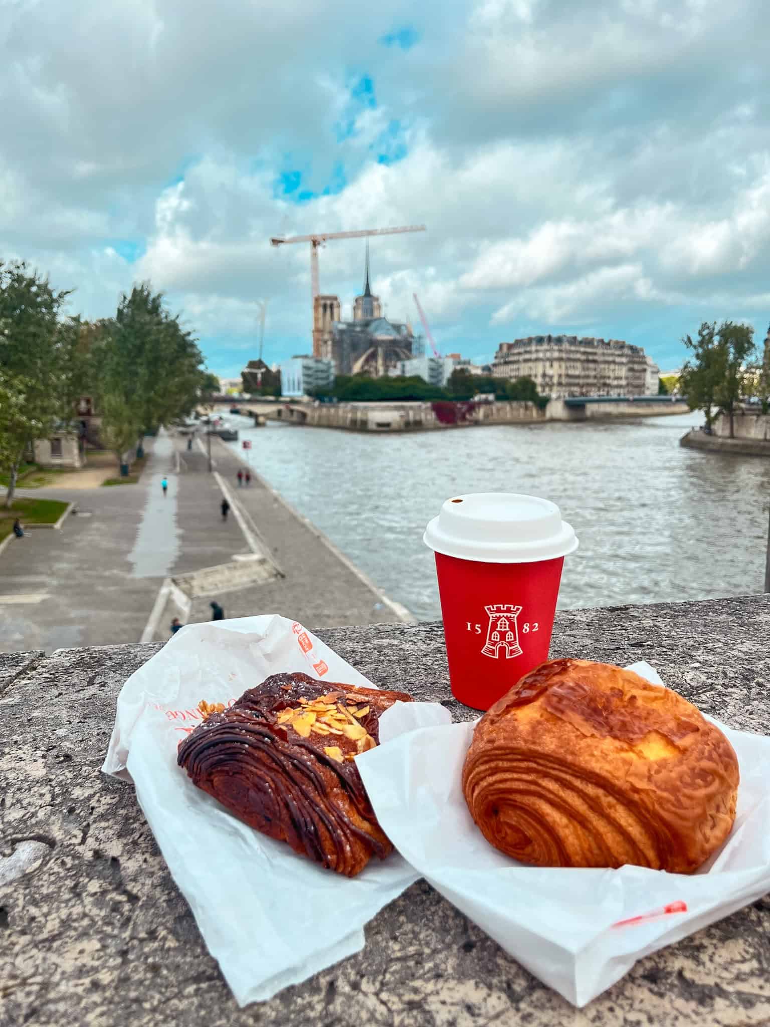 Fresh French pastries including pain au chocolat and croissant by the Seine River, quintessential things to do in Paris food experiences