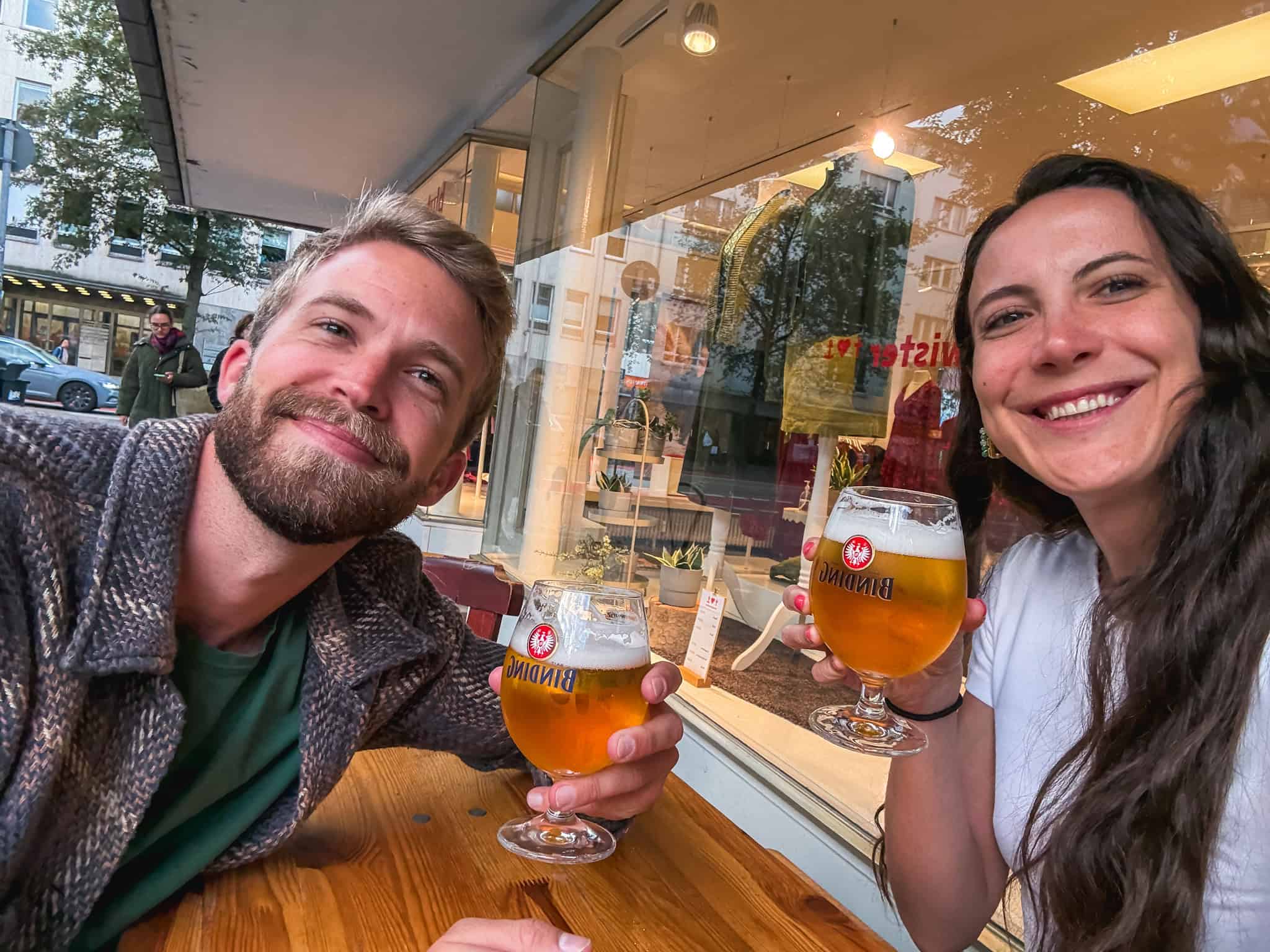 Couple toasting with Binding beer at a cozy Frankfurt cafe, enjoying local breweries during one day in Frankfurt