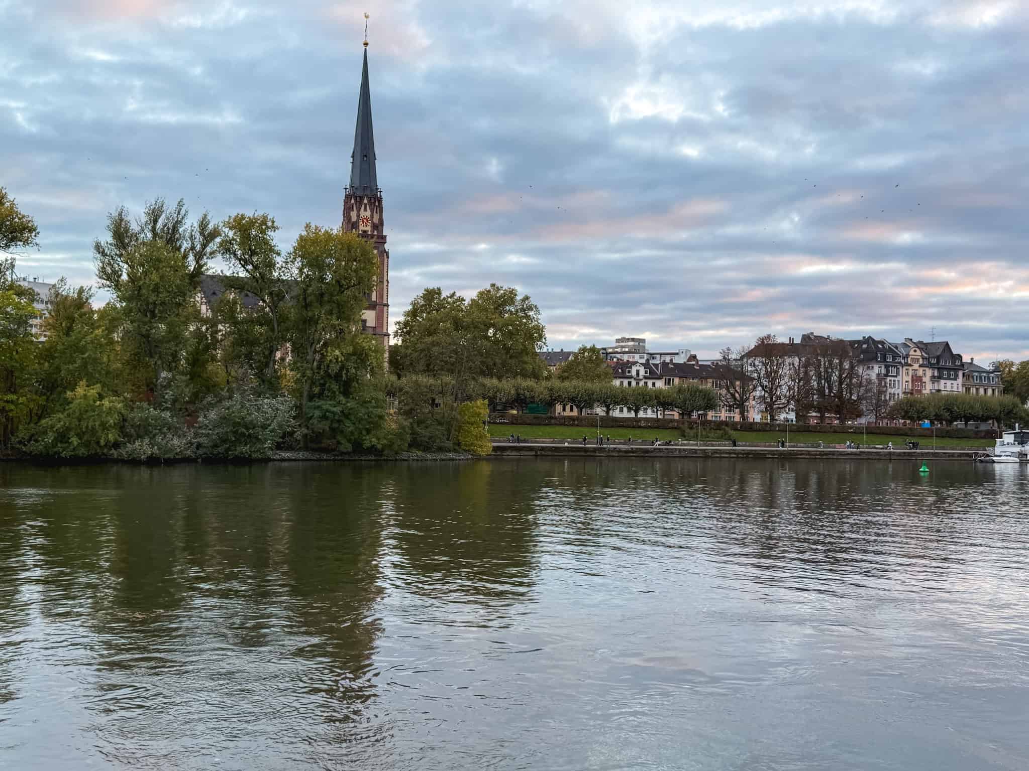 Tranquil Main River view with church spire and autumn foliage, peaceful walking route for one day in Frankfurt