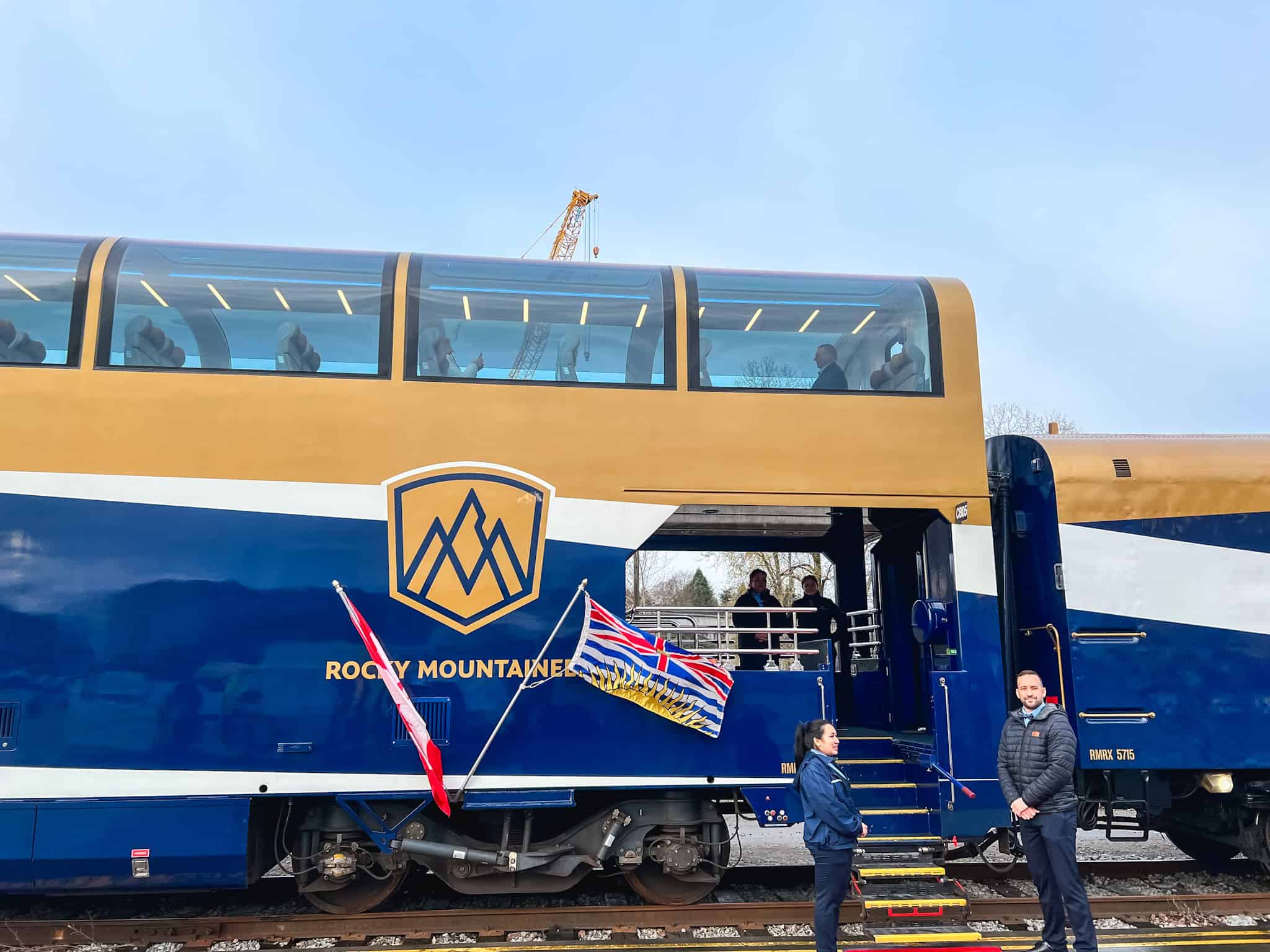 Rocky Mountaineer train exterior showing iconic gold and blue GoldLeaf service coaches with glass-dome windows and Canadian flags at station