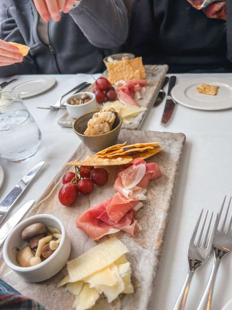 Gourmet charcuterie board with prosciutto, artisan cheese, grapes, crackers, and marinated mushrooms served during scenic train journey