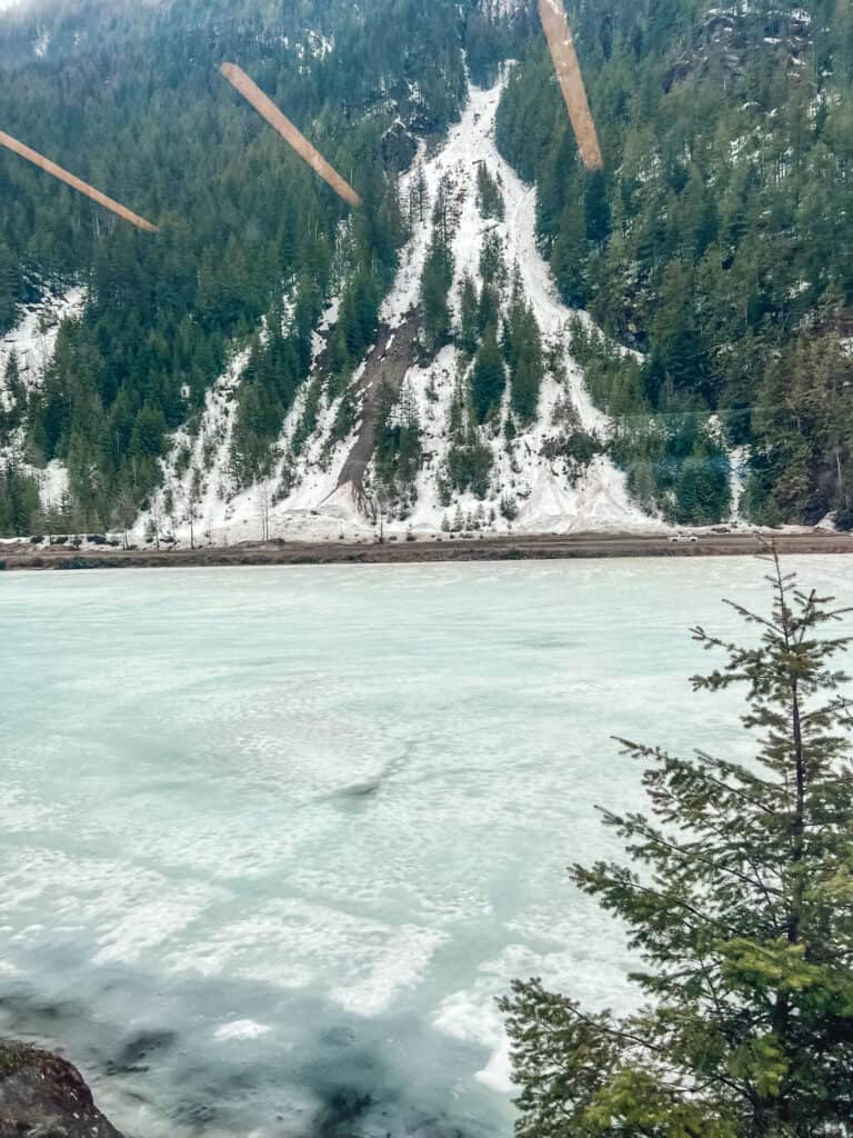 Frozen turquoise river with avalanche chutes and snow-covered mountains along scenic railway route in winter