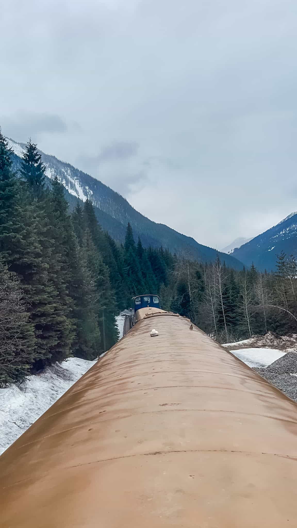 Rocky Mountaineer train exterior showing gold-topped GoldLeaf coaches curving through snowy mountain valley on Vancouver to Kamloops route