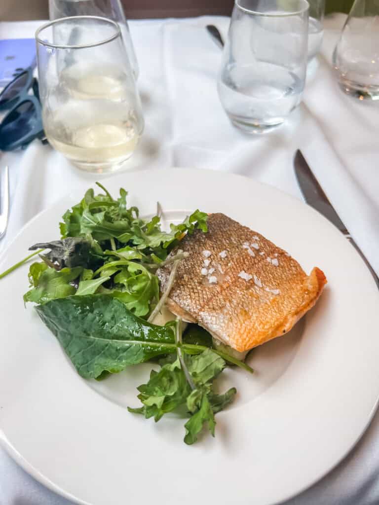 Pan-seared Pacific salmon with arugula salad and white wine served during GoldLeaf luxury train dining experience