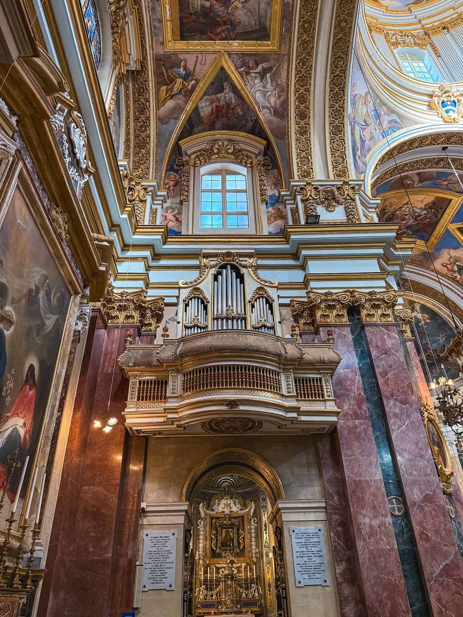 Ornate baroque church interior in Malta with golden decorations, frescoed ceiling, and historic pipe organ