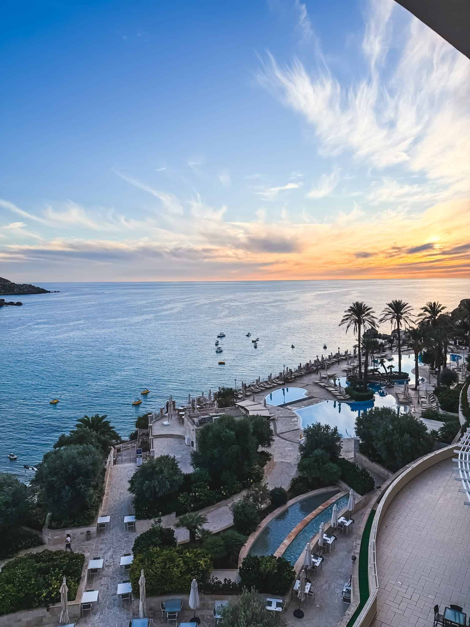 Luxury Malta beachfront hotel at sunset with infinity pools, palm trees, and Mediterranean Sea views