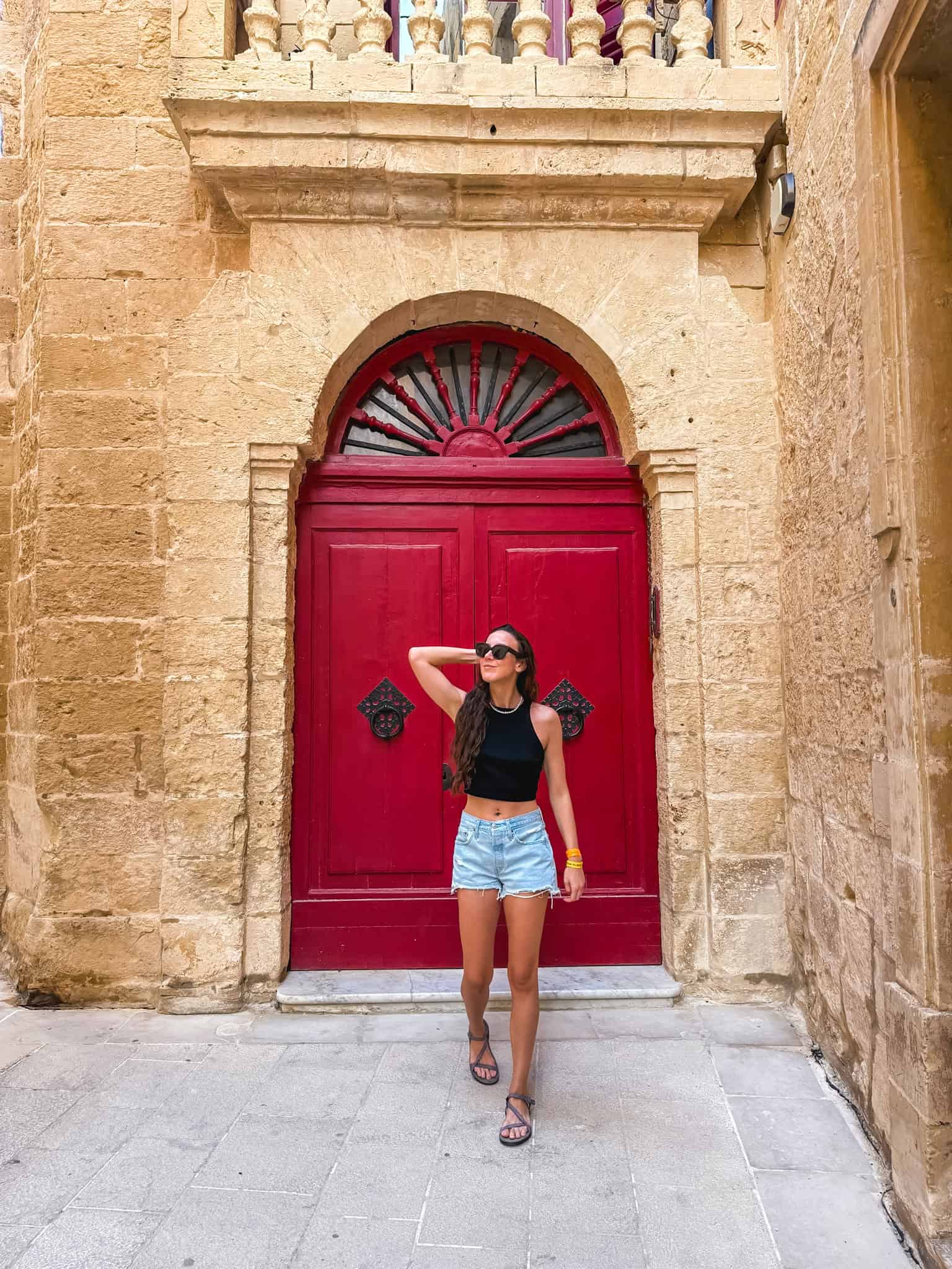 Traveler posing at traditional red Maltese door in historic old town streets perfect for Malta photography
