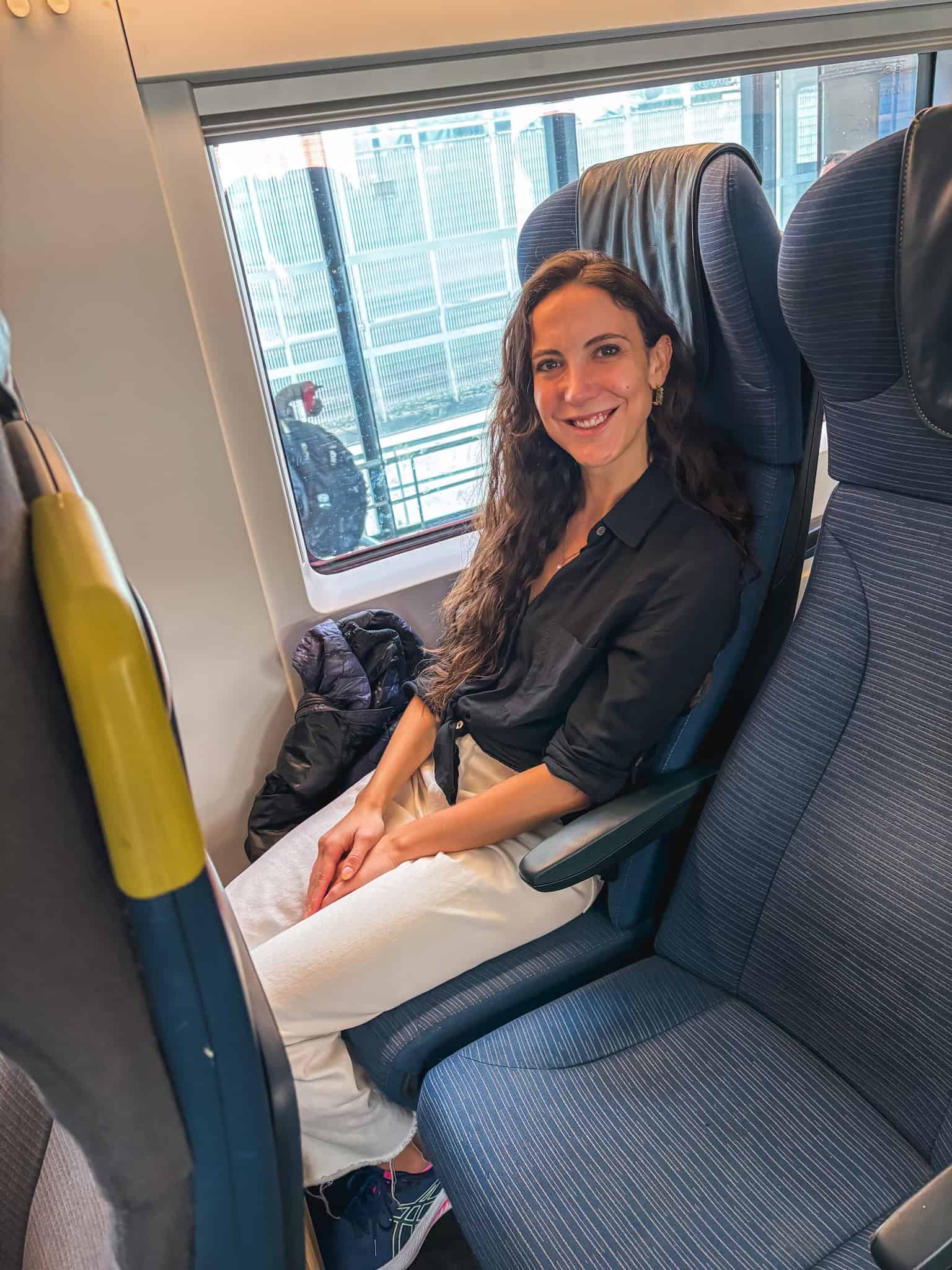 A woman smiling in her seat by the window aboard the Eurostar while enjoying the train from paris to london on a sunny day
