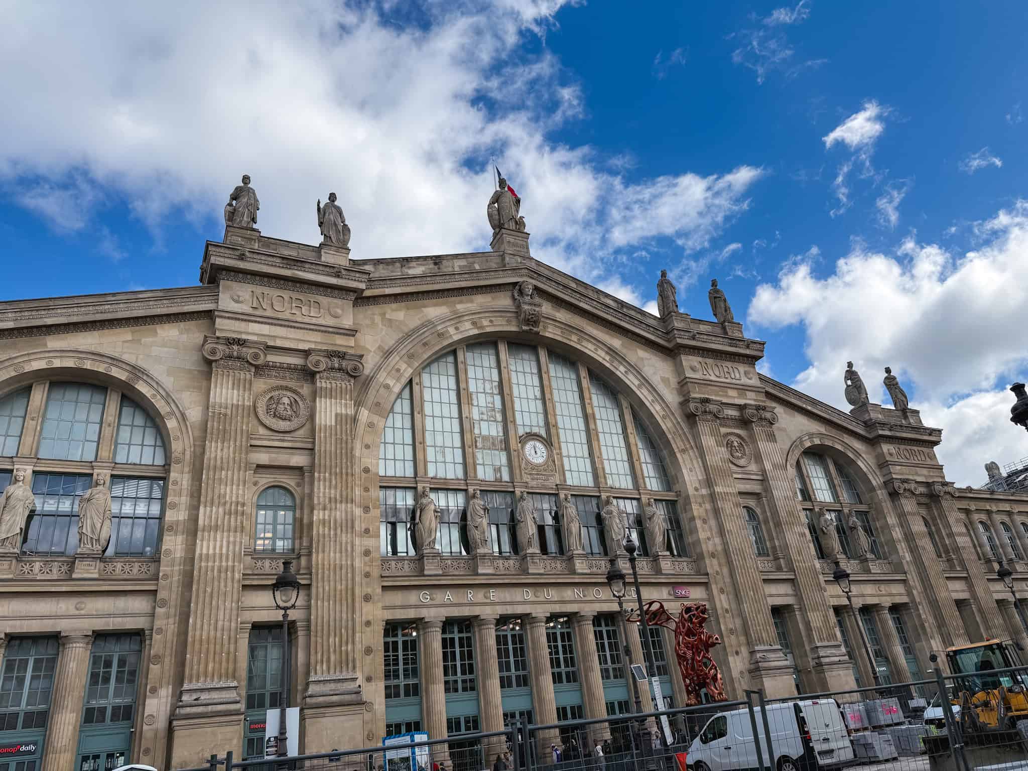 The iconic Beaux-Arts exterior of Gare du Nord in Paris featuring classical columns, stone statues, and a central clock above the main entrance