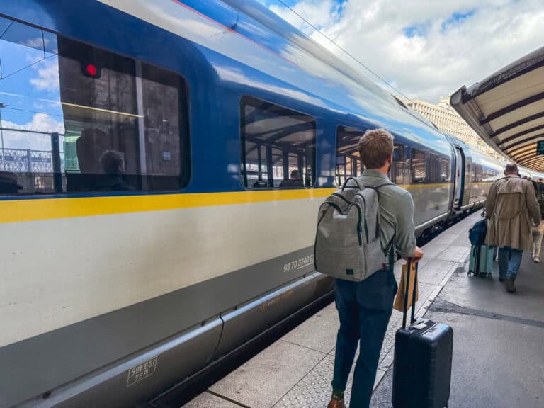 A backpacker with rolling luggage standing on the platform next to a blue and yellow Eurostar carriage ready to board the train from paris to london